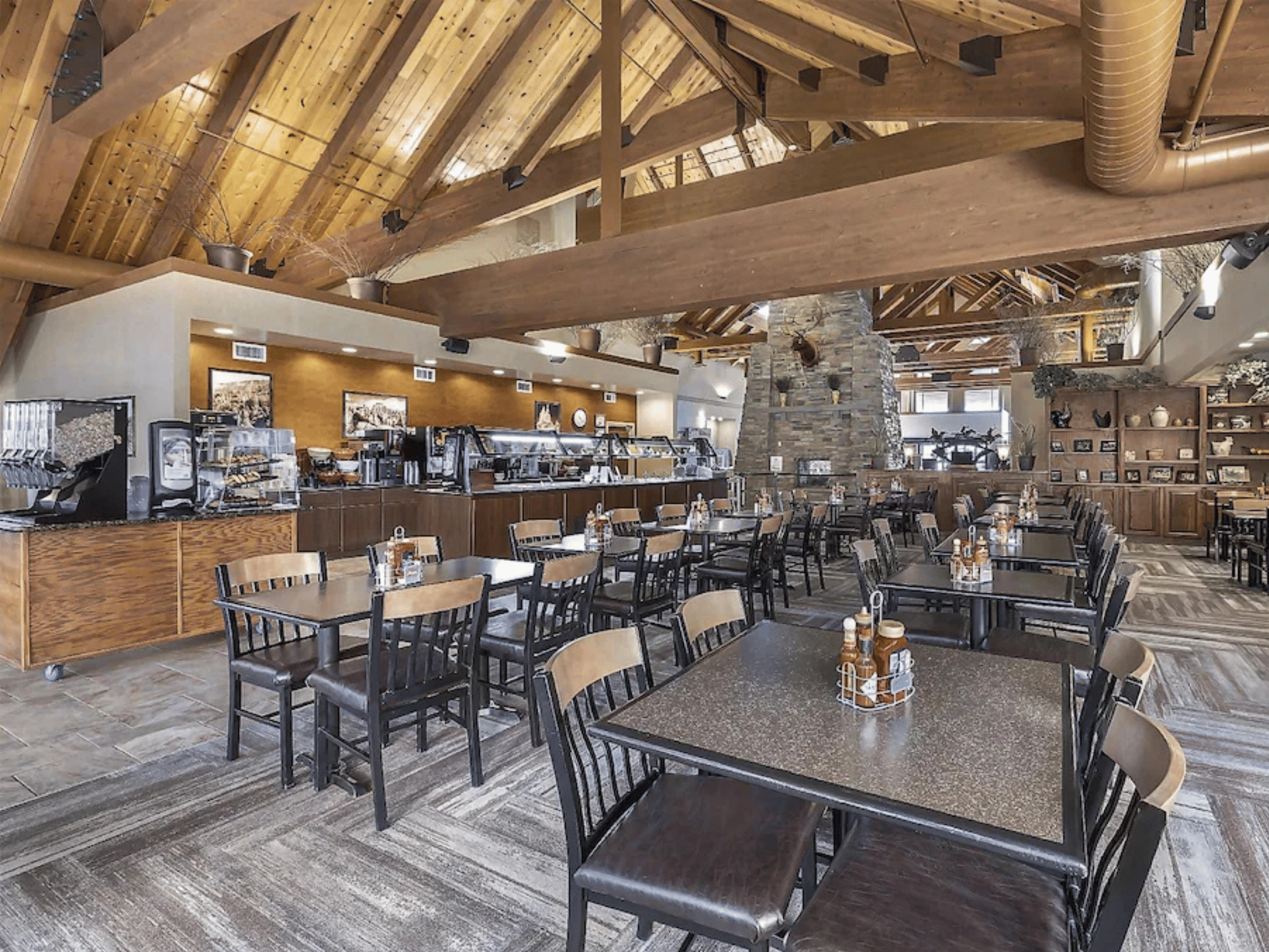 Spacious lodge dining hall with vaulted timber truss ceilings, stone fireplace, buffet service counter, and table seating