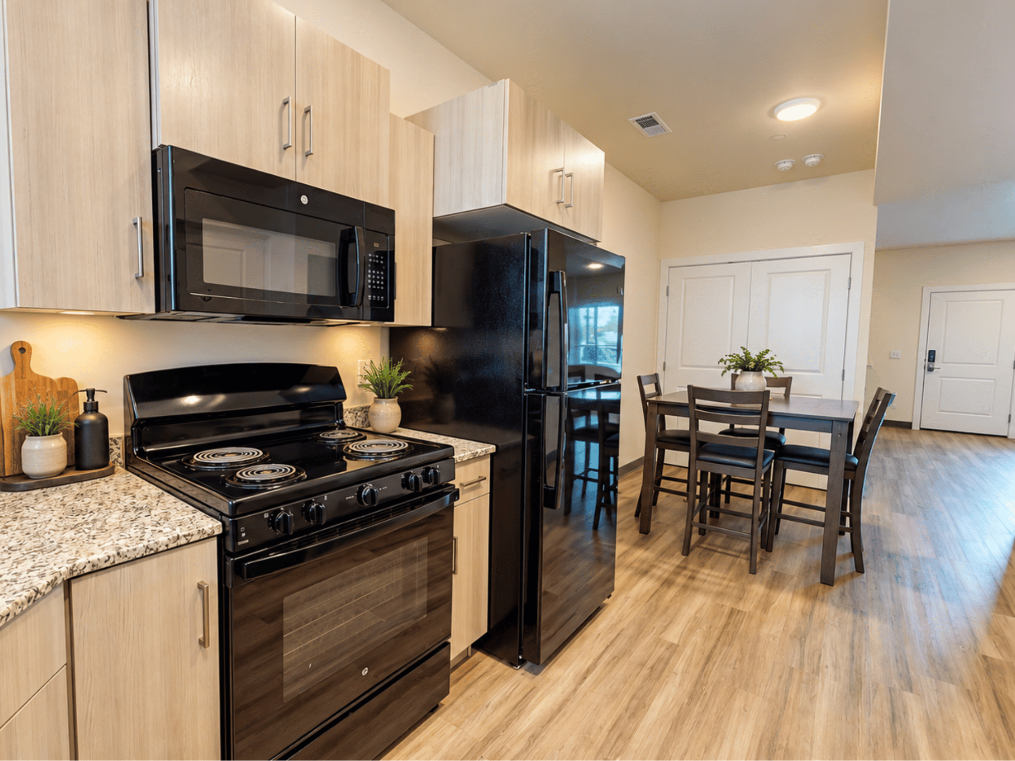 Modern apartment kitchen and dining area featuring two-tone cabinetry, black appliances, granite-style countertops, and wood-look plank flooring
