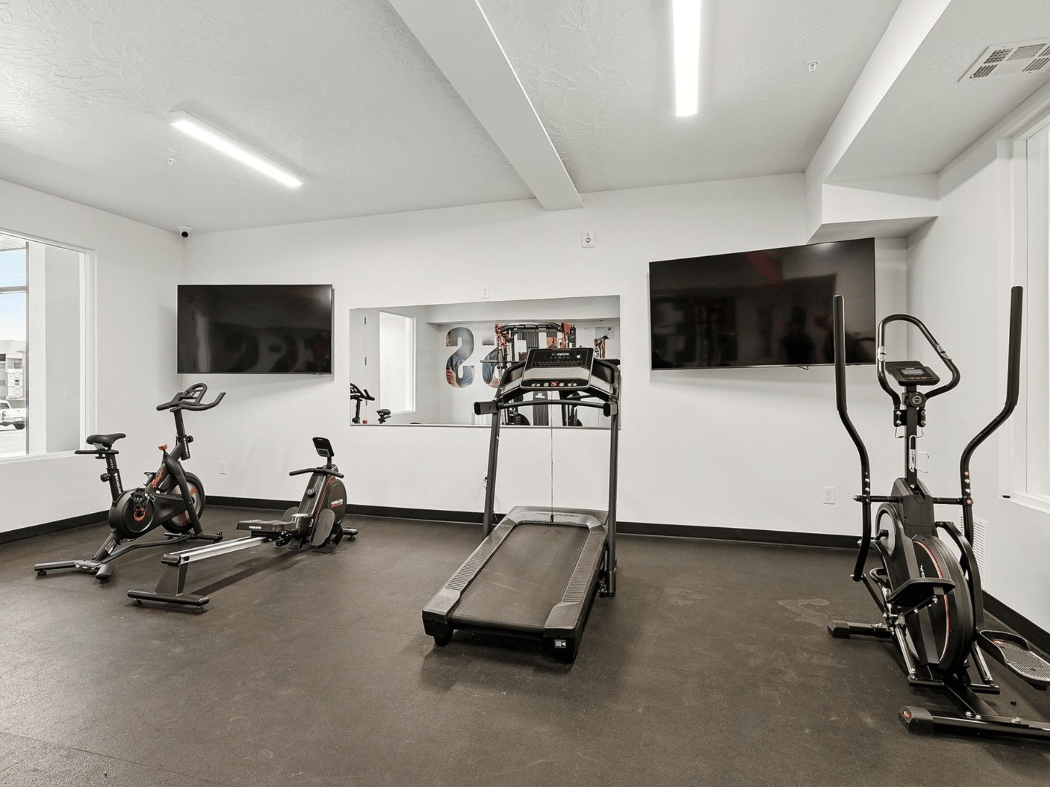 Fitness center cardio room featuring treadmill, exercise bikes, rowing machine, and wall-mounted monitors
