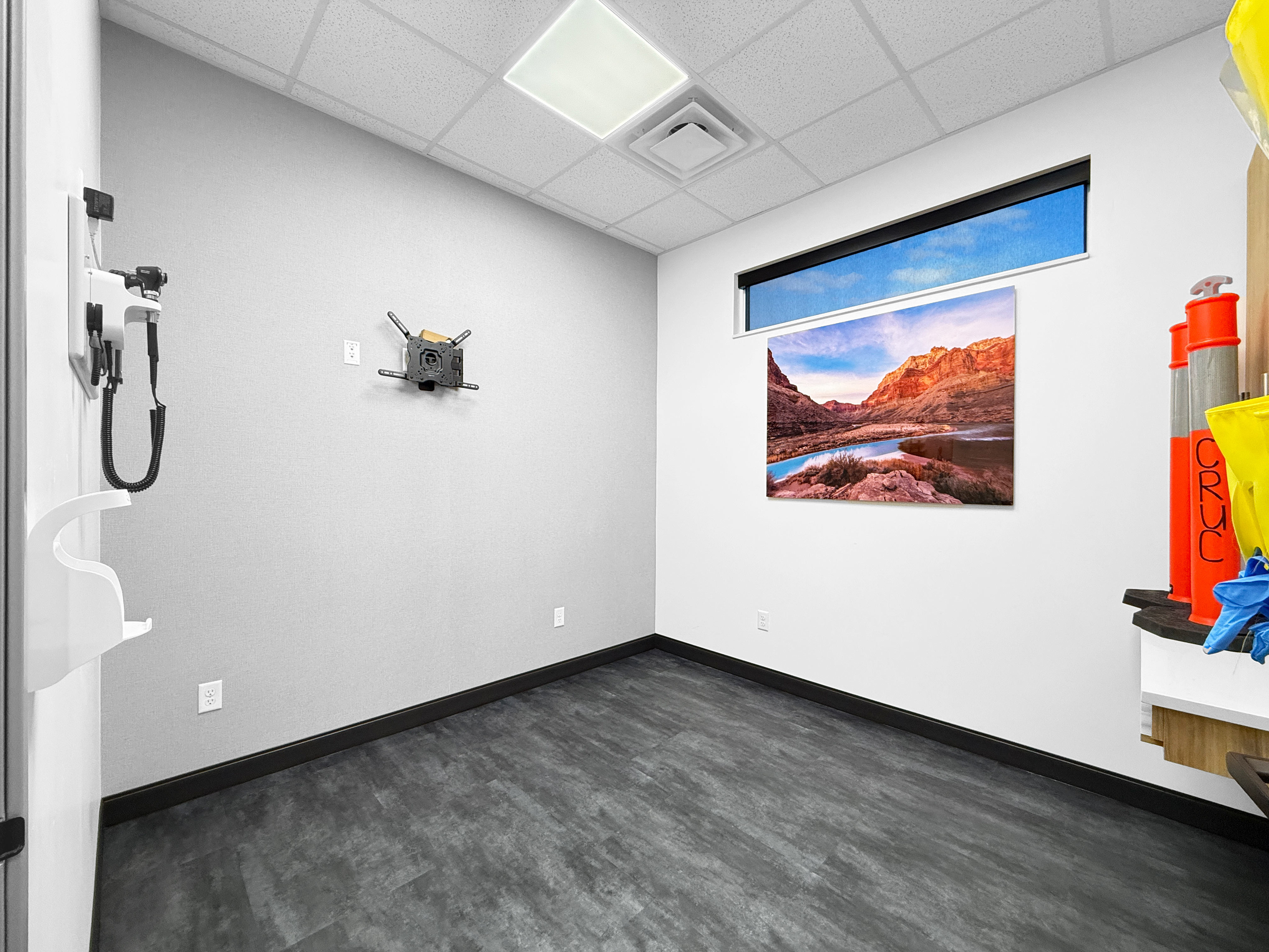 Clinical exam room with wall-mounted diagnostic equipment, clerestory window, and red rock wall art