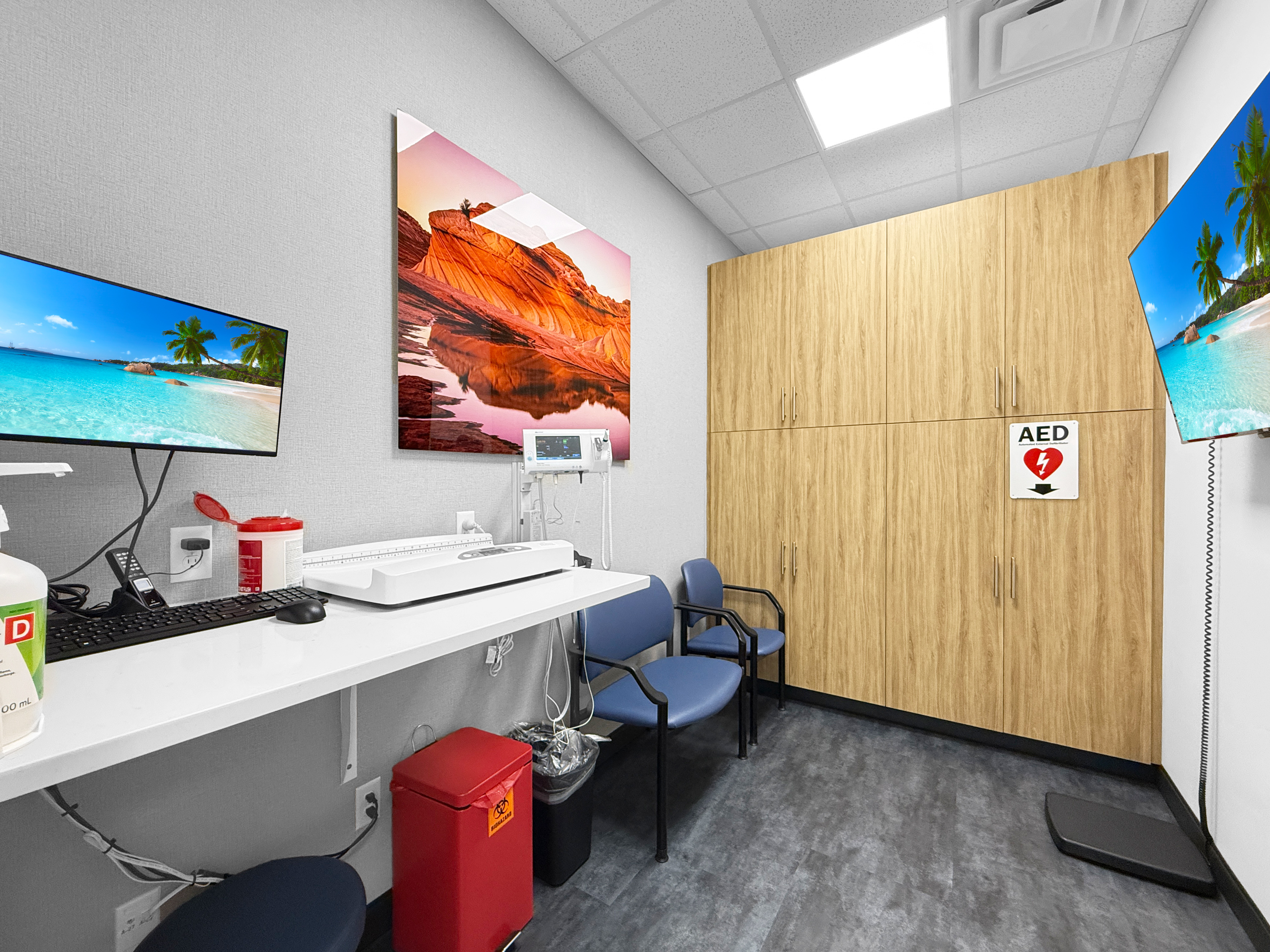 Medical exam and triage room with custom wood-grain cabinetry, patient examination bench, computer workstation, and AED station