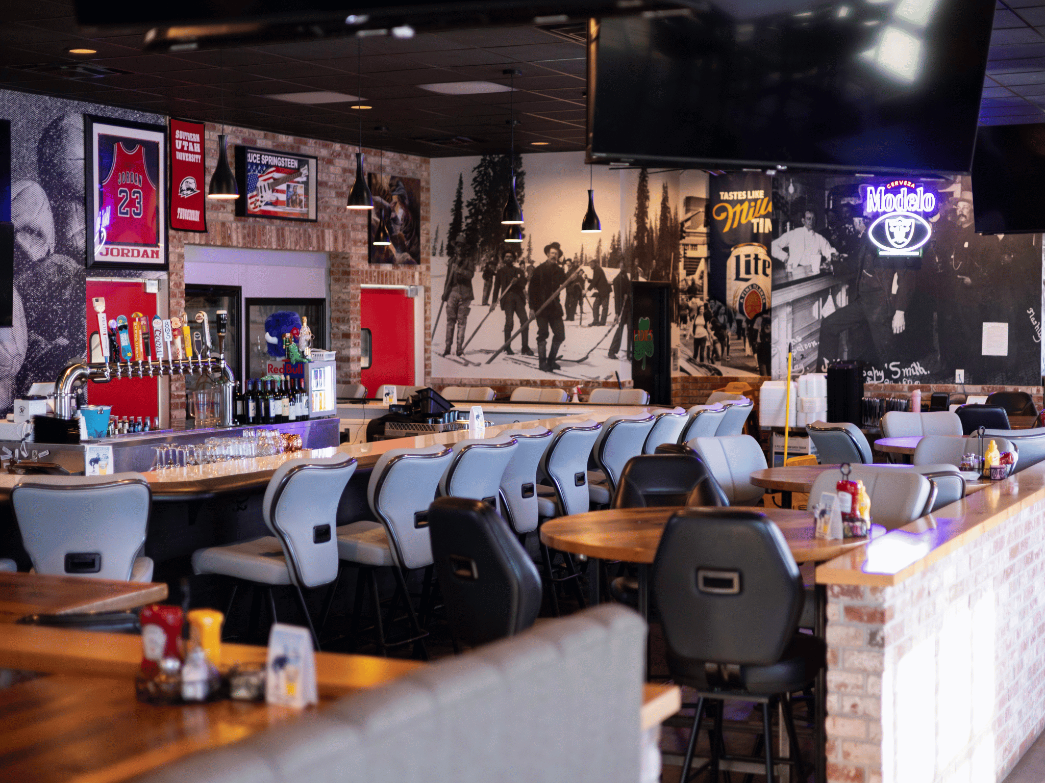 Full bar counter with padded barstools, draft beer tap tower, neon signage, and historical wall murals