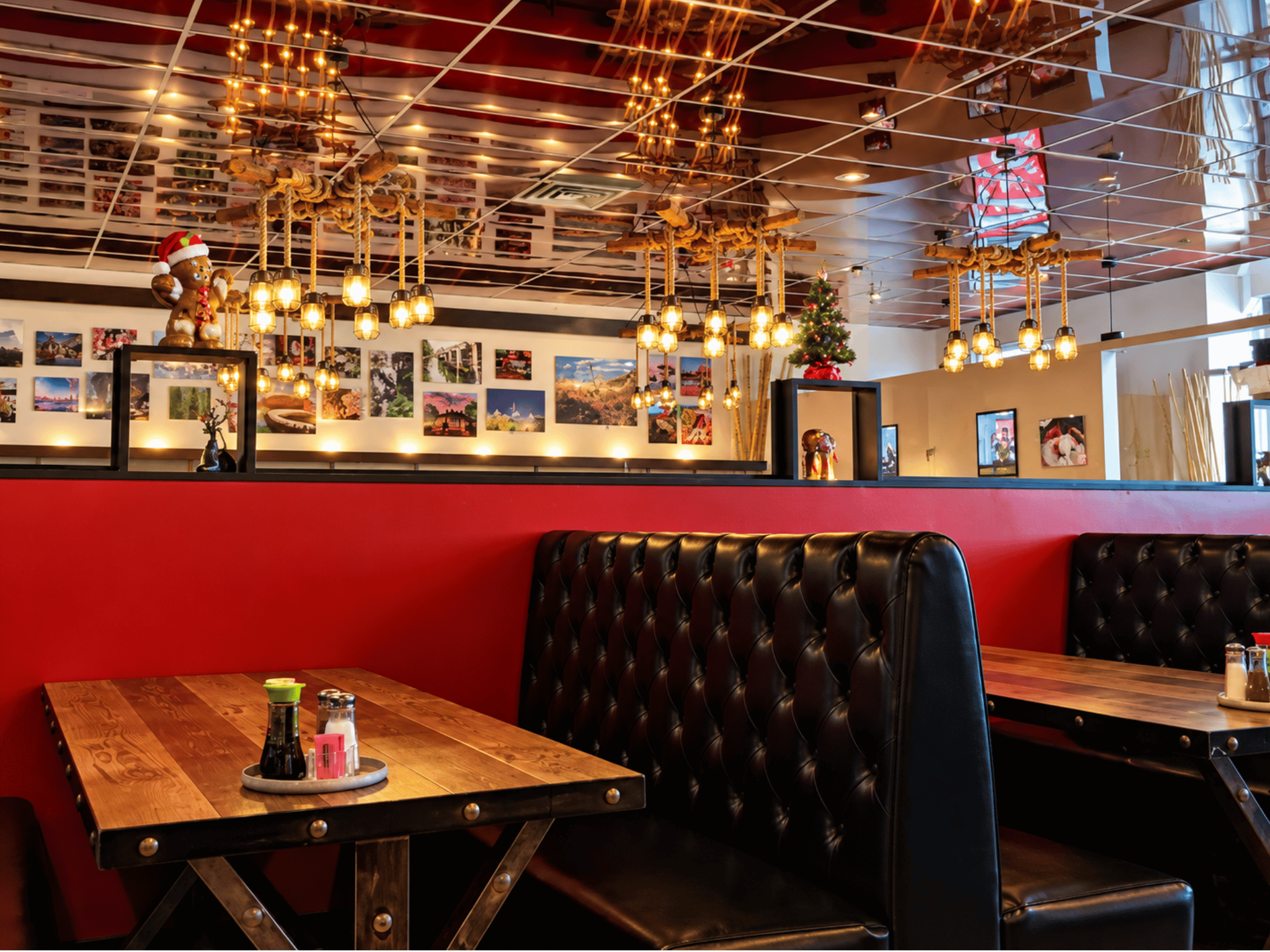 Dining room booth with tufted leather seating, rustic wood-and-steel table, bold red walls, and decorative rope pendant lighting