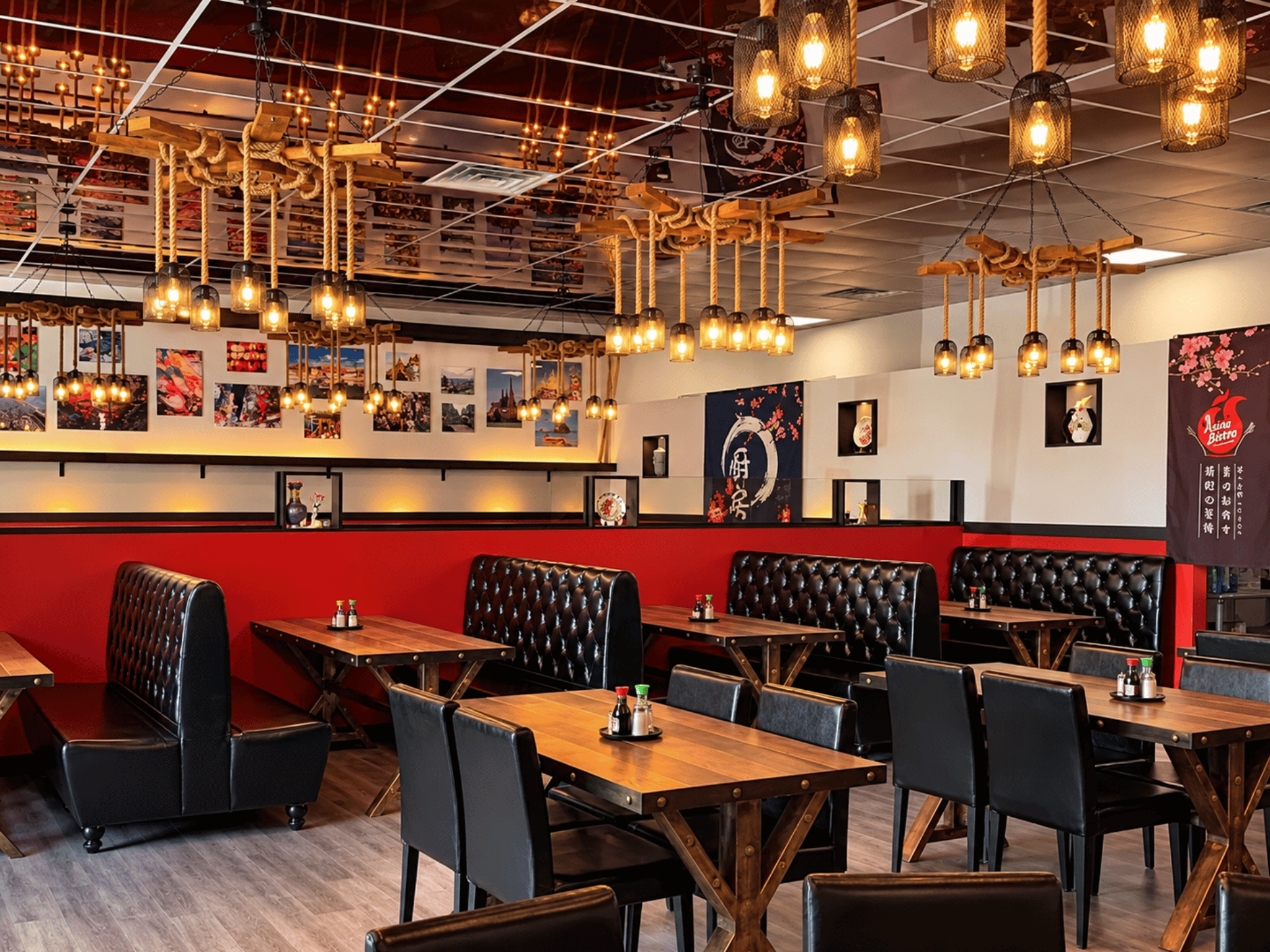 Spacious main dining room at Asian Bistro with red accent walls, tufted booth seating, custom pendant chandeliers, and hardwood-look flooring