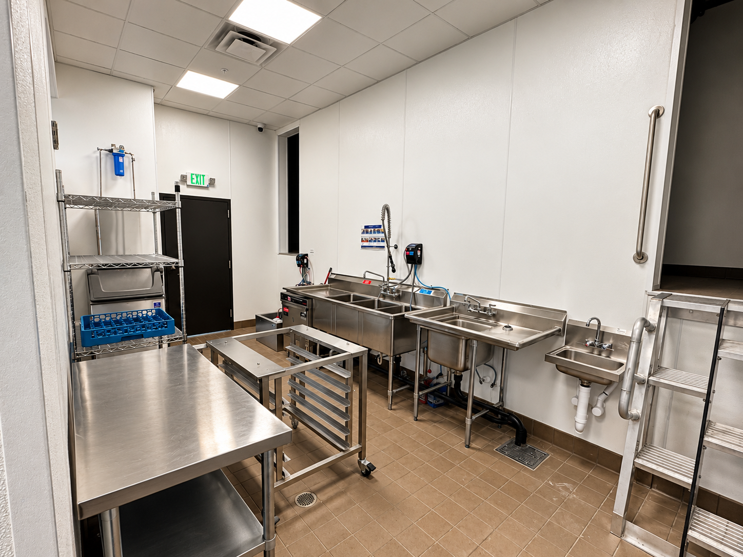 Commercial kitchen dishwashing and food prep area with multi-compartment stainless steel sinks and work tables at Abbey Inn