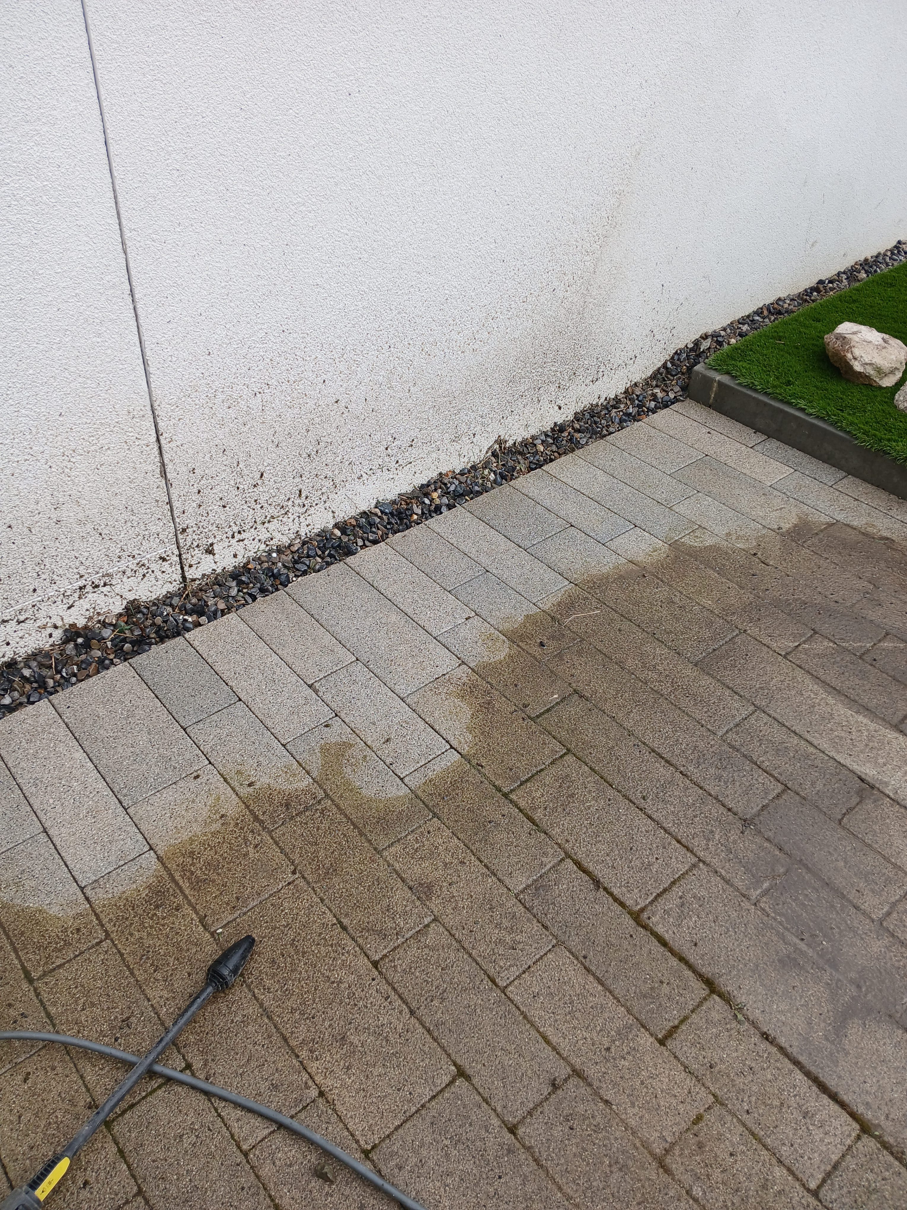 Before and after power washing on block paving patio in a South Dublin garden, showing dramatic contrast between deep clean stone and mossy weathered surface.