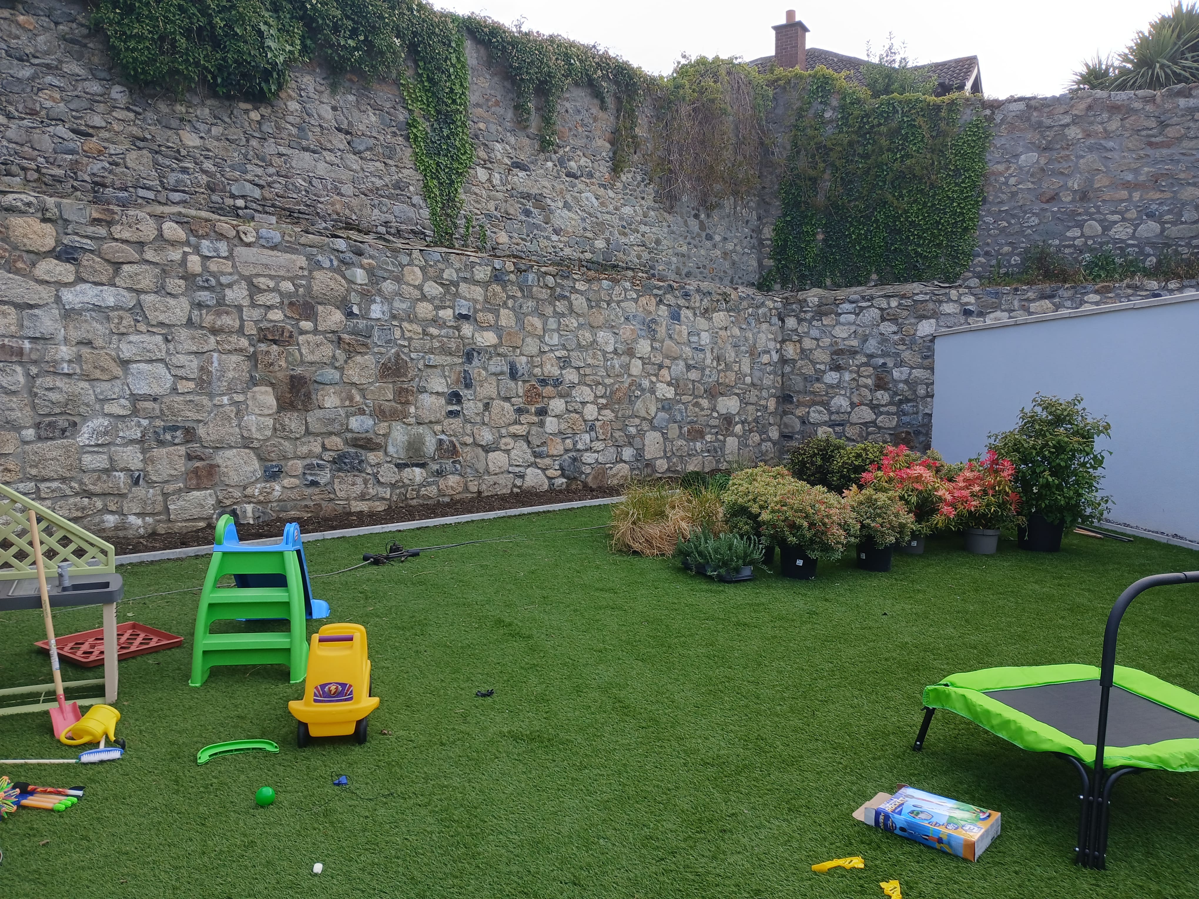 Expansive view of multi-tiered Irish granite boundary wall with staged border planting and family lawn in South Dublin.