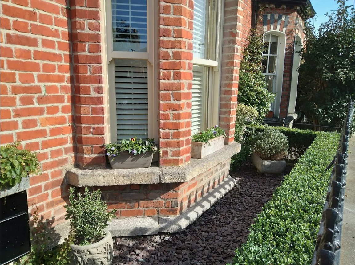 Period red brick bay window frontage featuring manicured box hedge, planted window boxes and dark decorative stone mulch in Blackrock, Dublin South Side.