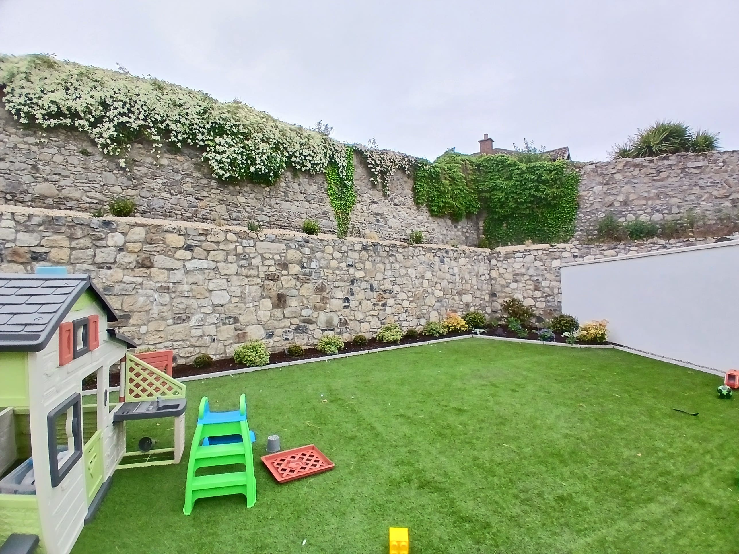 Completed planting and bark mulched border along a magnificent tiered granite stone wall crowned with flowering clematis in a South Dublin garden.