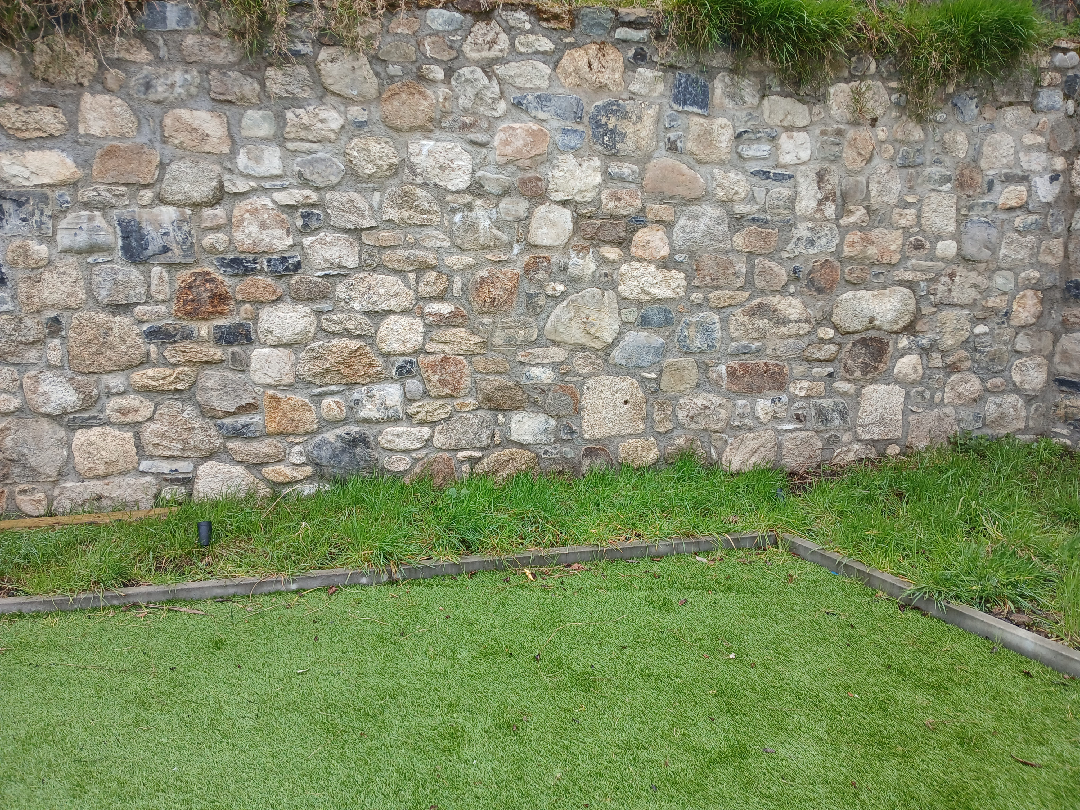 Initial lawn preparation stage showing rustic stone wall, overgrown edging and ground levelling in Dublin South Side.