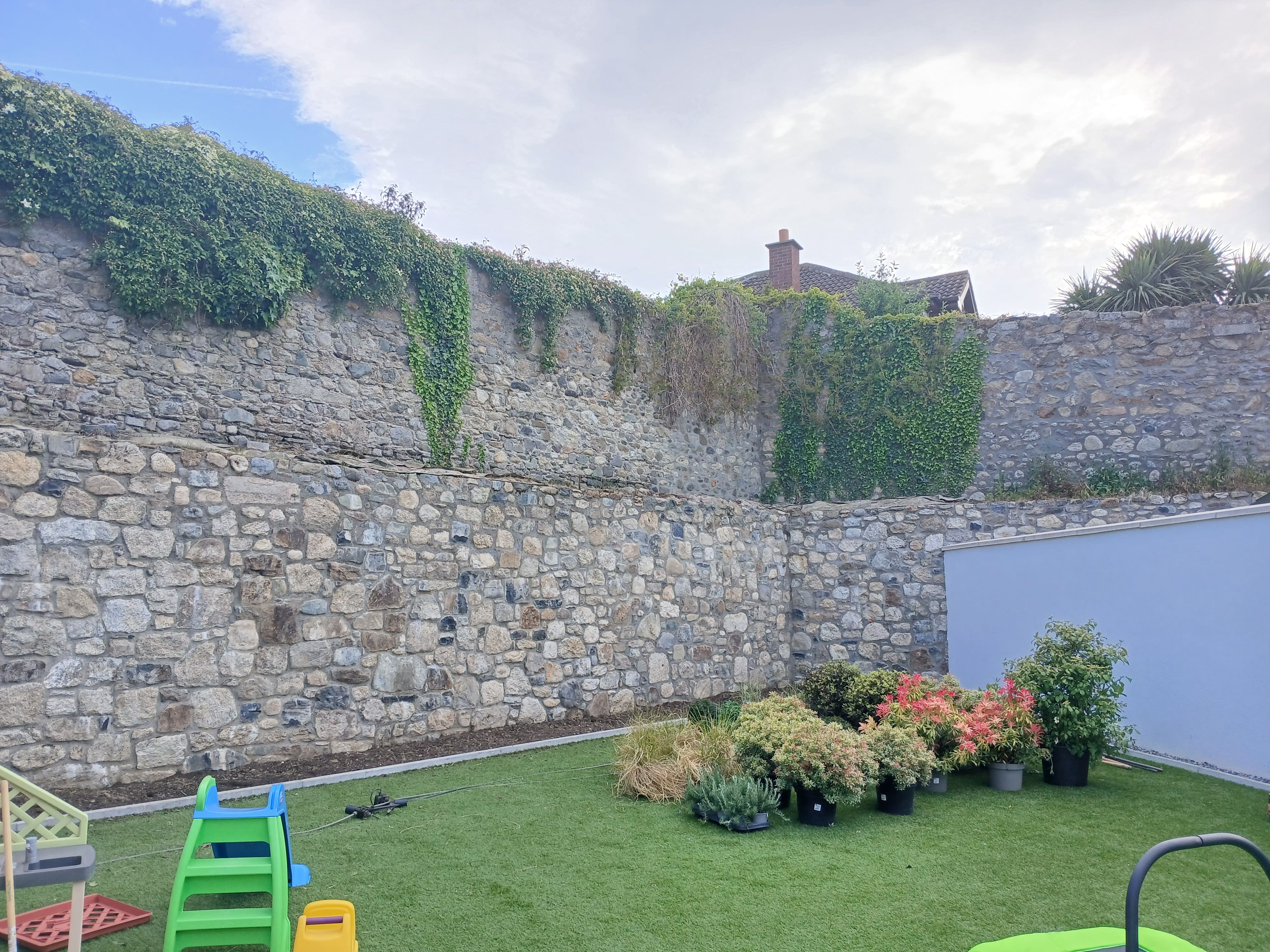 Lawn boundary and family play area alongside dramatic tiered historic granite stone wall in a Dublin South Side residence.