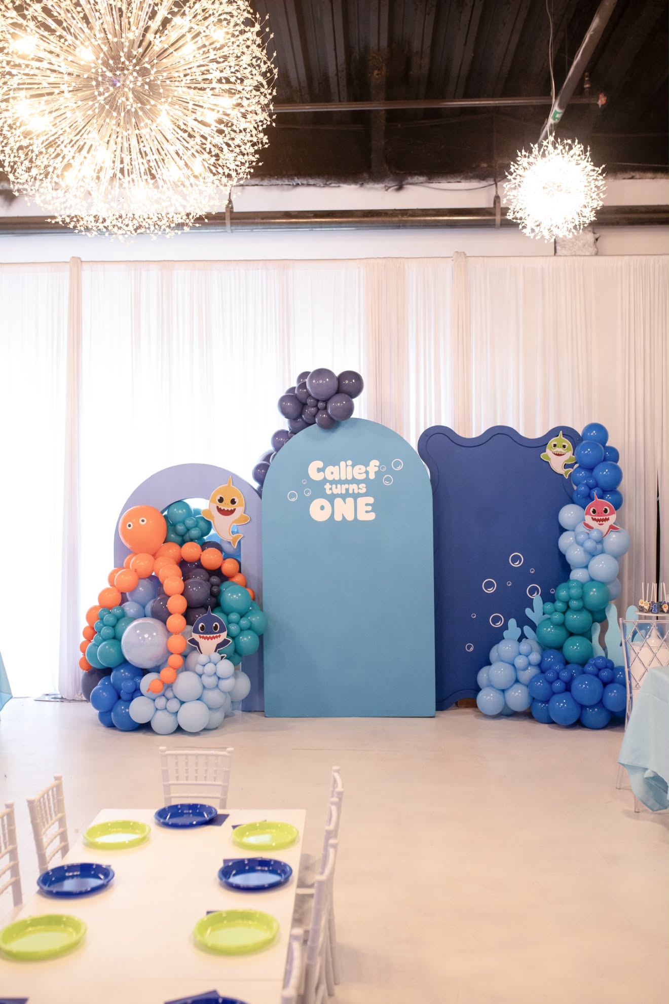 Custom ocean blue arched backdrops, multi-toned balloon installations, and children's table seating