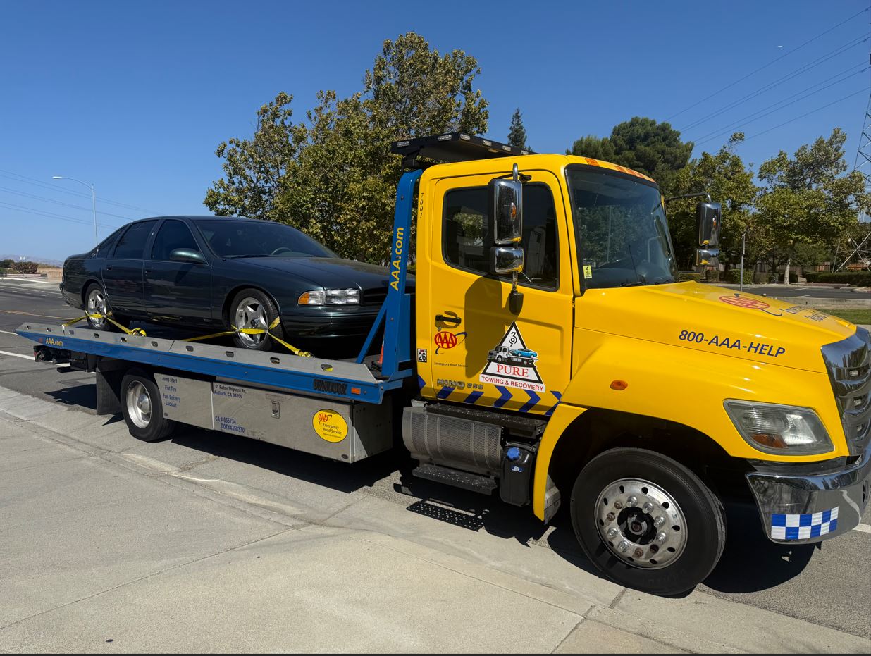 Pure Towing & Recovery commercial Hino 258 rollback flatbed carrier with Pure door logo transporting a classic sedan secured with yellow tire straps