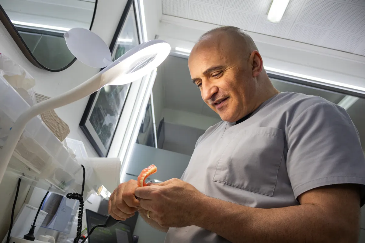 Dental prosthetist inspecting a denture under a magnifying lamp at Preston Dentures