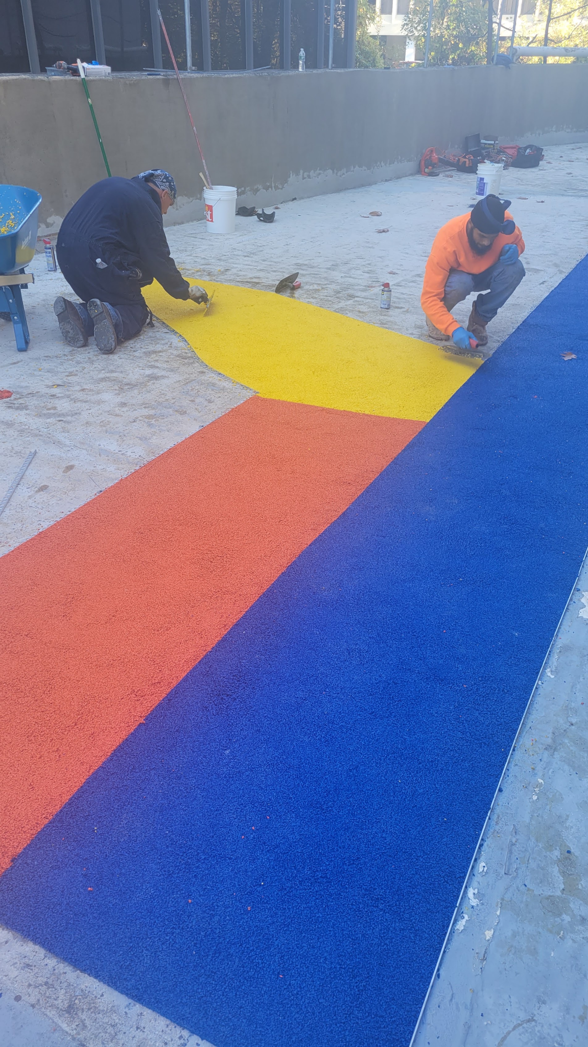 Hudson Epoxy Flooring installers actively hand-troweling sharp geometric yellow, orange, and blue floor coating