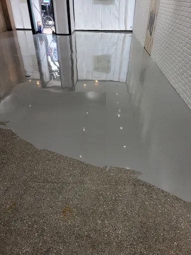 Hudson Epoxy Flooring completed high-gloss gray floor coating transitioning cleanly into a full decorative flake floor section against white brick wall