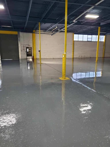 Hudson Epoxy Flooring completed high-gloss gray concrete floor coating in large commercial warehouse facility with yellow steel support columns