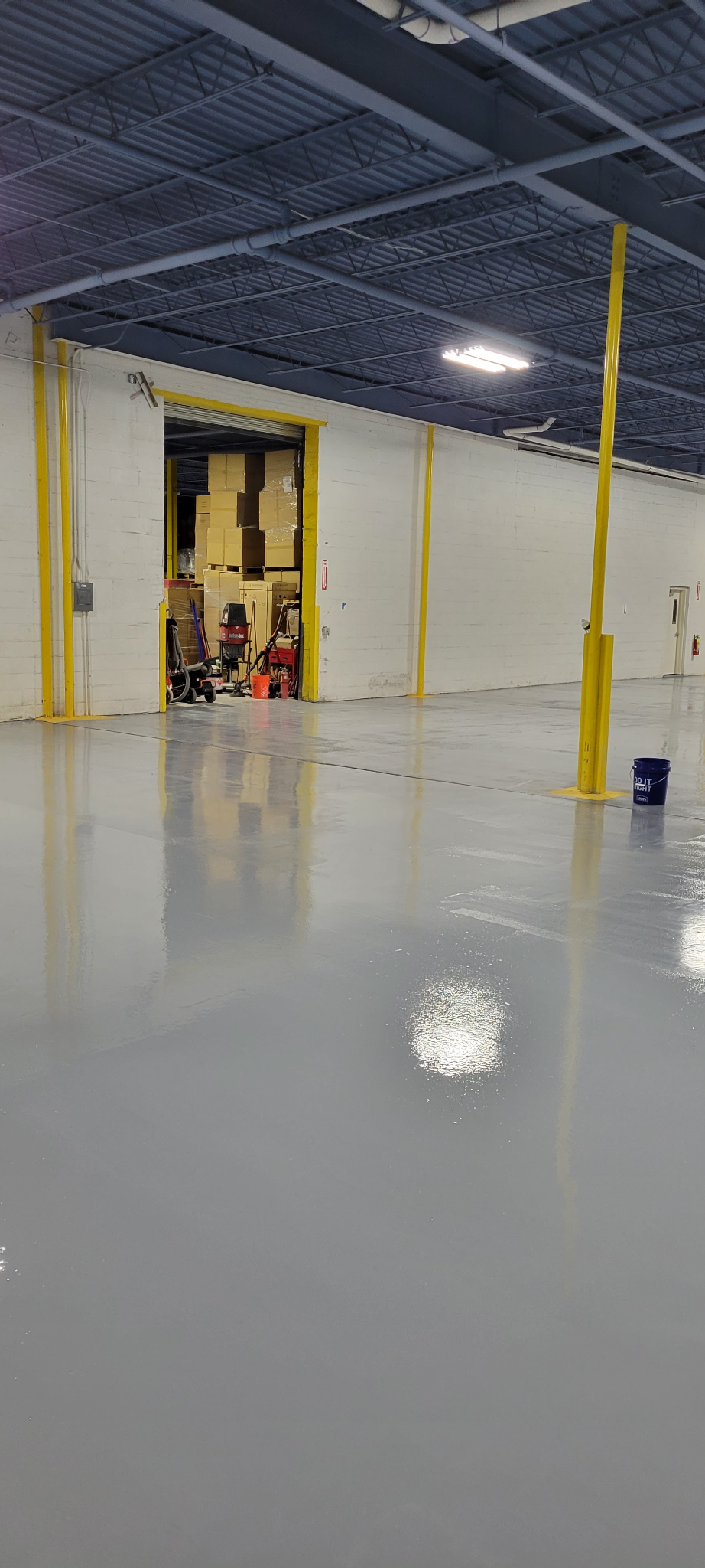 Hudson Epoxy Flooring completed high-gloss gray concrete floor coating in large commercial warehouse facility with yellow structural columns