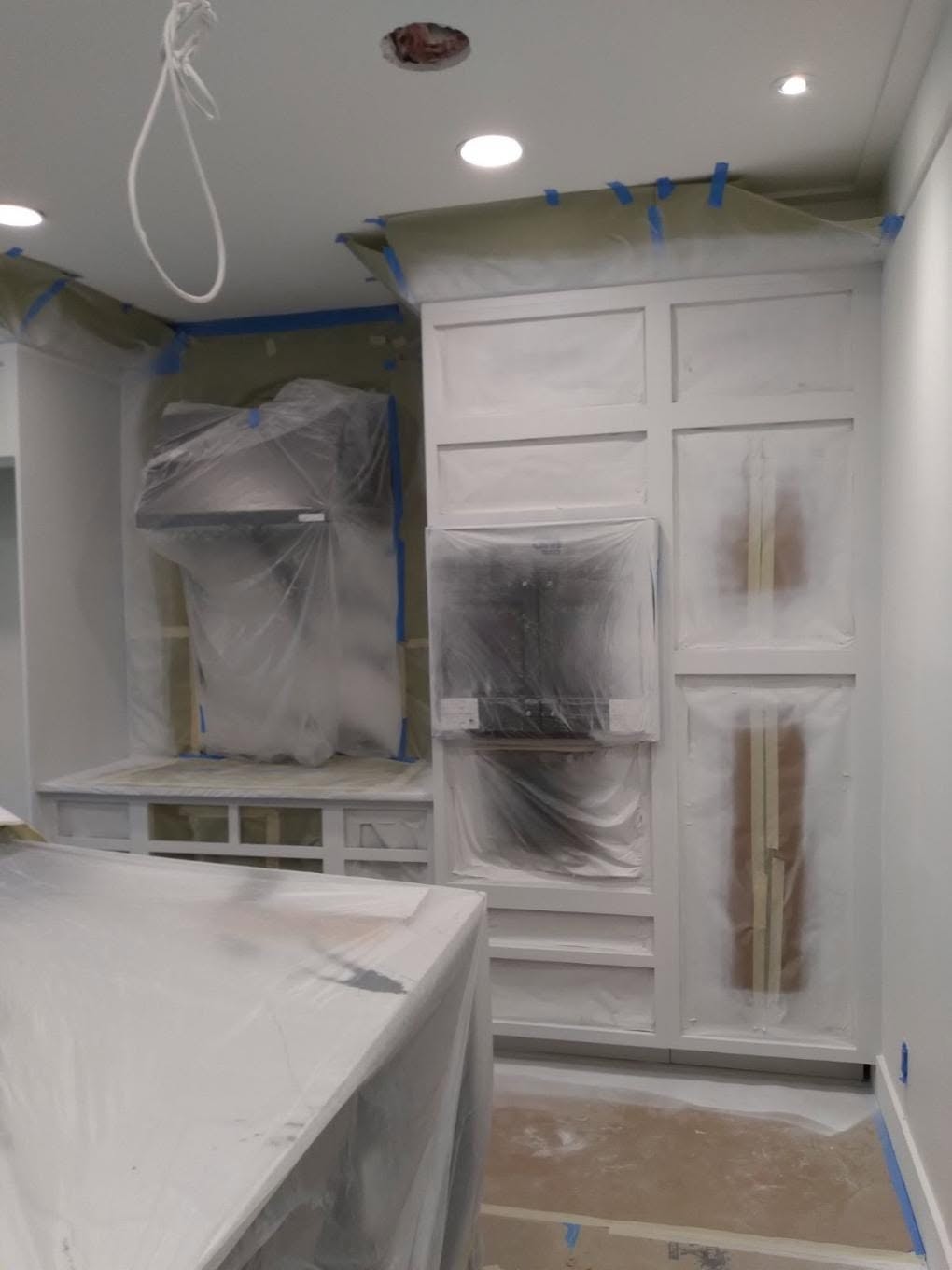 Kitchen island, countertops, and appliances sealed in protective poly masking before cabinet spray painting in Naples