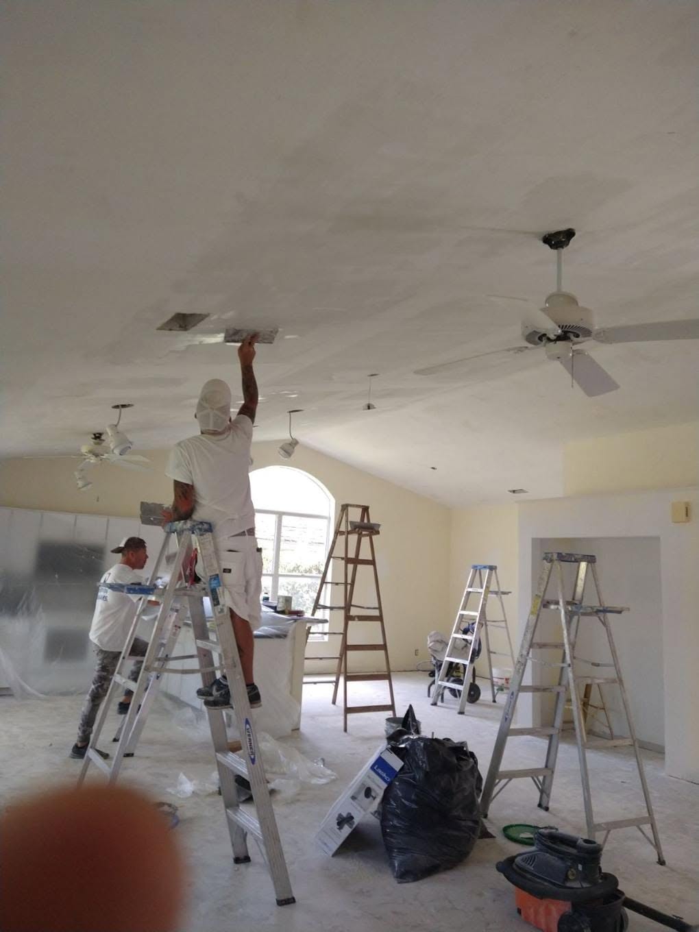 Painters on ladders applying smooth drywall compound skim coat on vaulted ceiling in Naples home