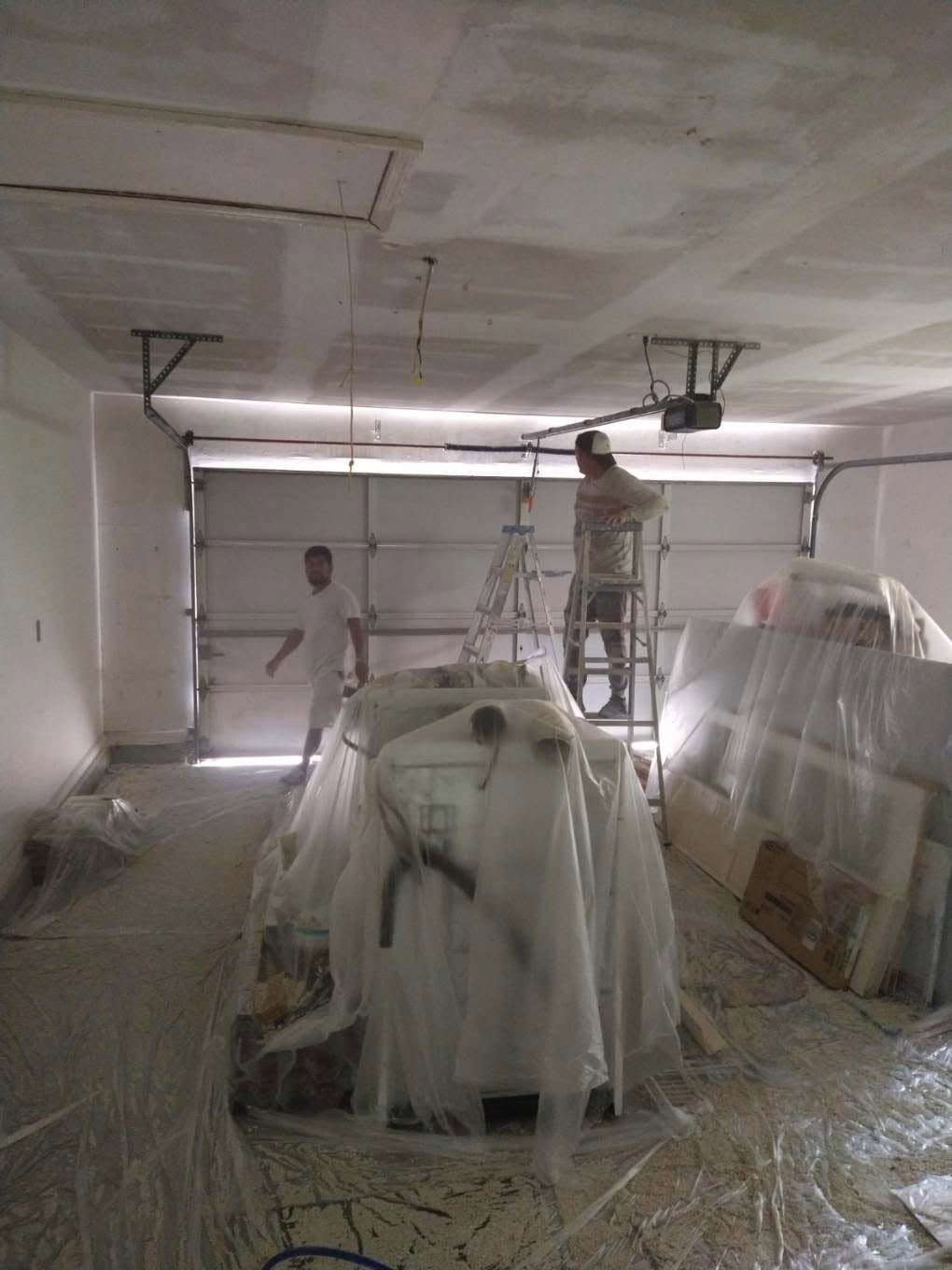 Garage interior sealed in poly drop plastic with painters staging ladders for ceiling drywall finishing in Naples