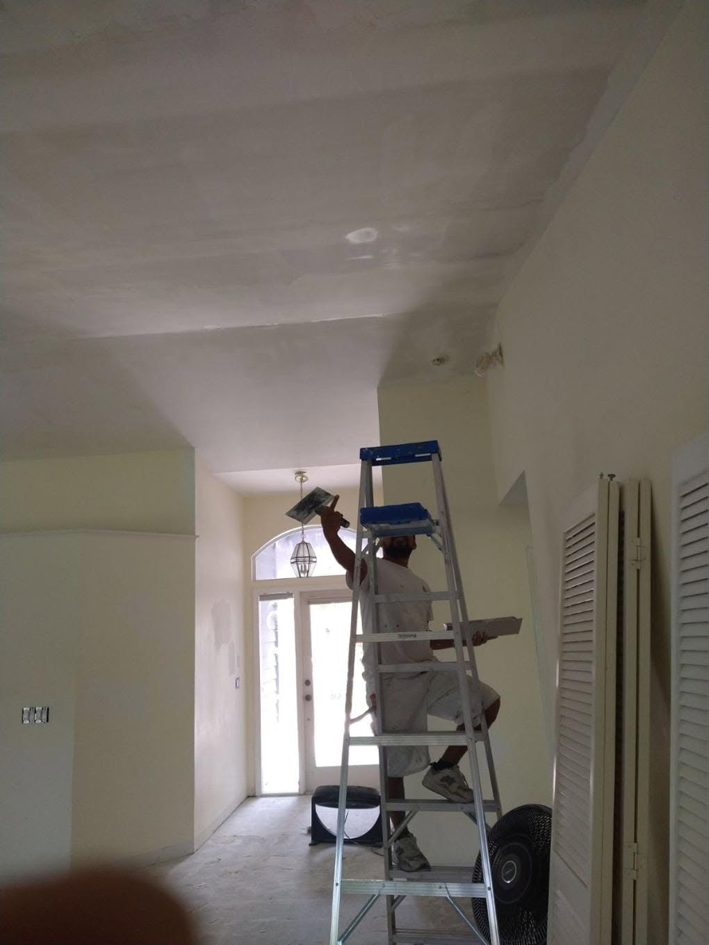 Finishing drywall skim coat on high ceiling entryway and arched transom in Naples home