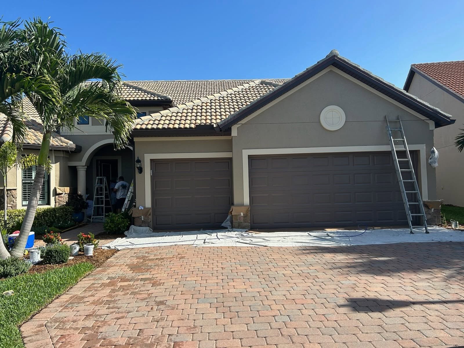 Tile-roof Naples home with paver driveway protected with drop cloths and ladders staged for exterior painting