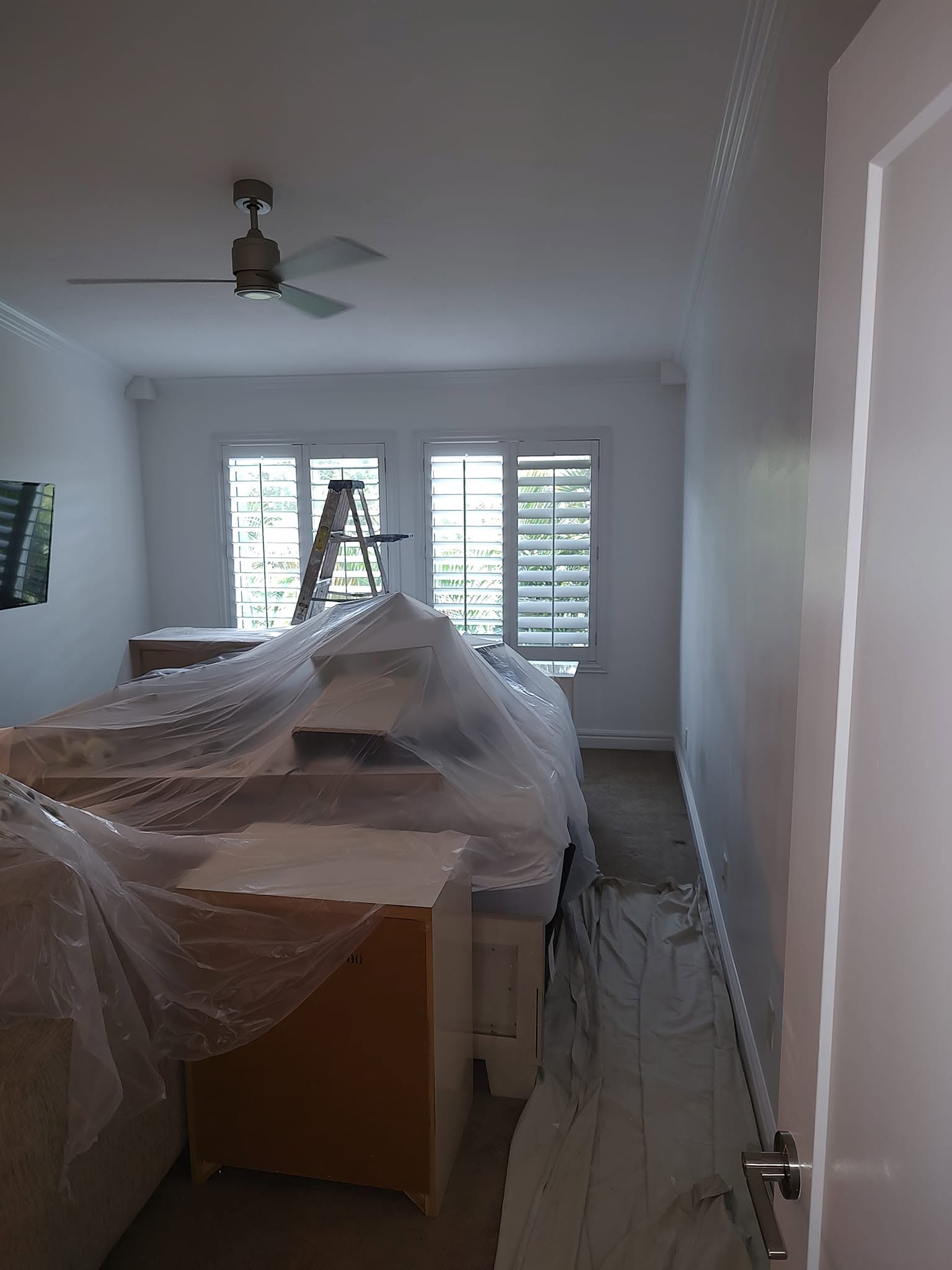 Bedroom furniture completely draped in protective plastic sheeting and carpet covered in drop cloths for interior painting in Naples