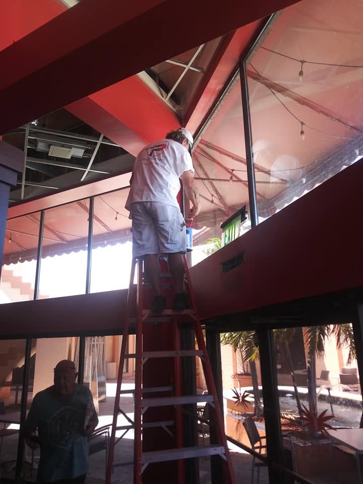 Commercial painter on ladder cutting in vibrant red structural headers and glass wall framing in Naples atrium