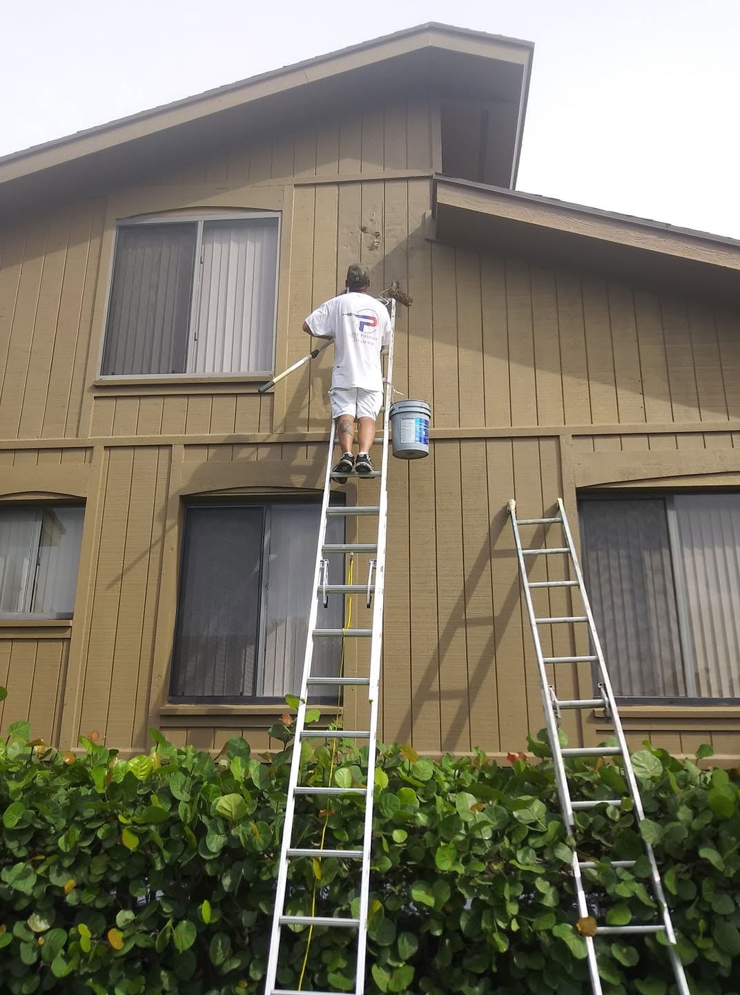 Painter on extension ladder rolling upper exterior siding on a two-story home in Naples