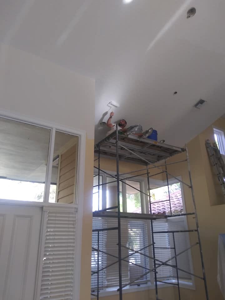 Painter on scaffold rolling soaring vaulted ceilings and tall foyer in Naples home