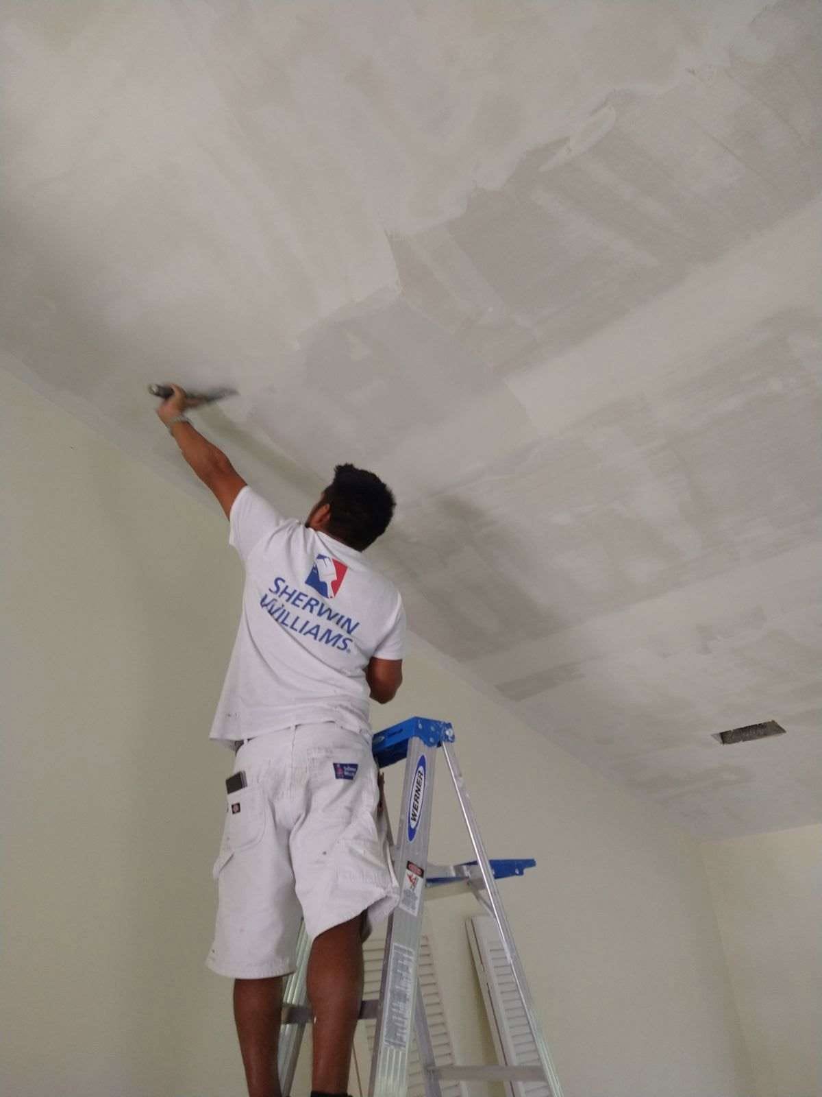 Professional painter on stepladder knife-smoothing ceiling joint compound in Naples