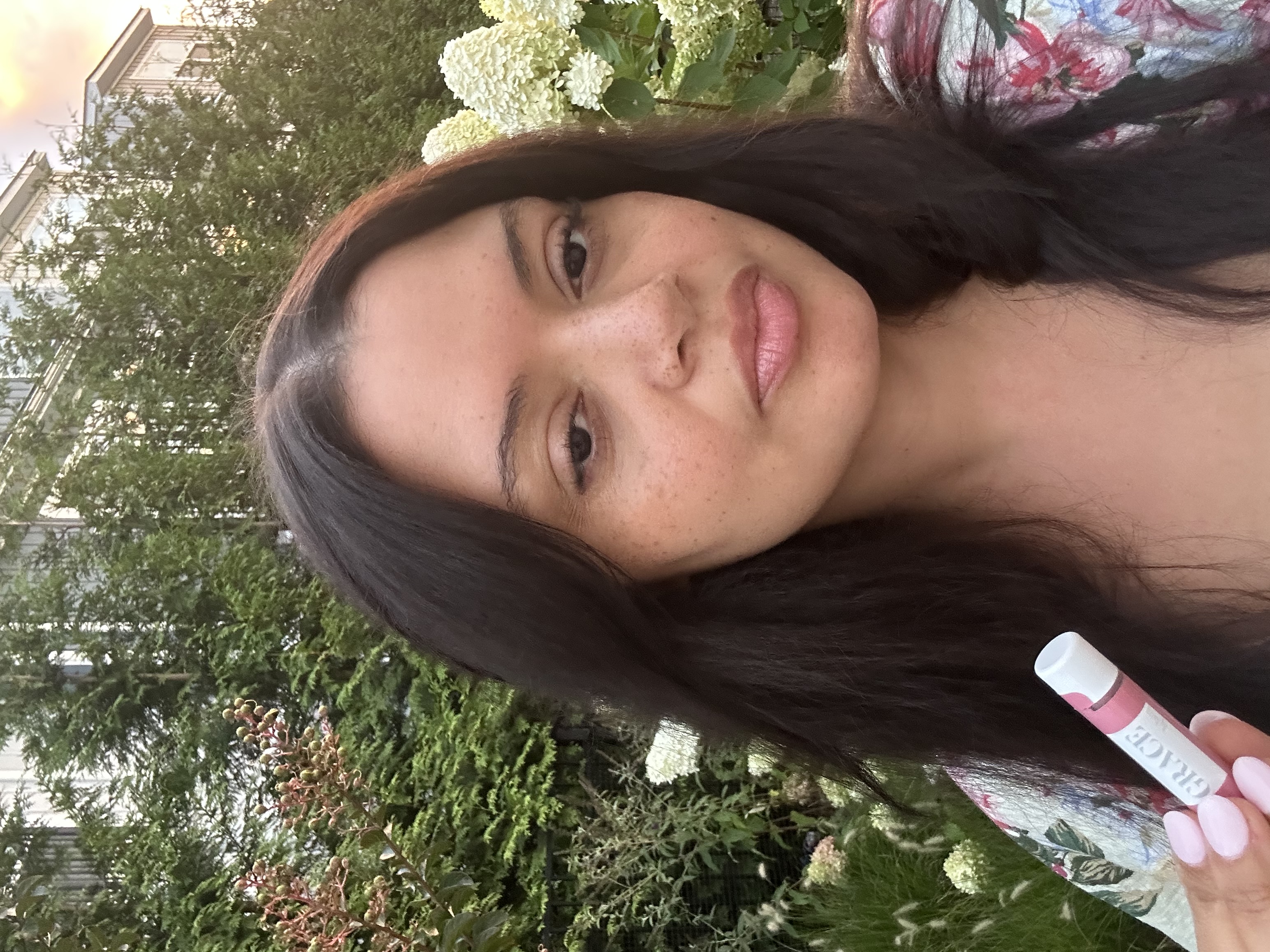 Founder Nazzy holding Grace by Nazzy lip balm in a serene outdoor setting