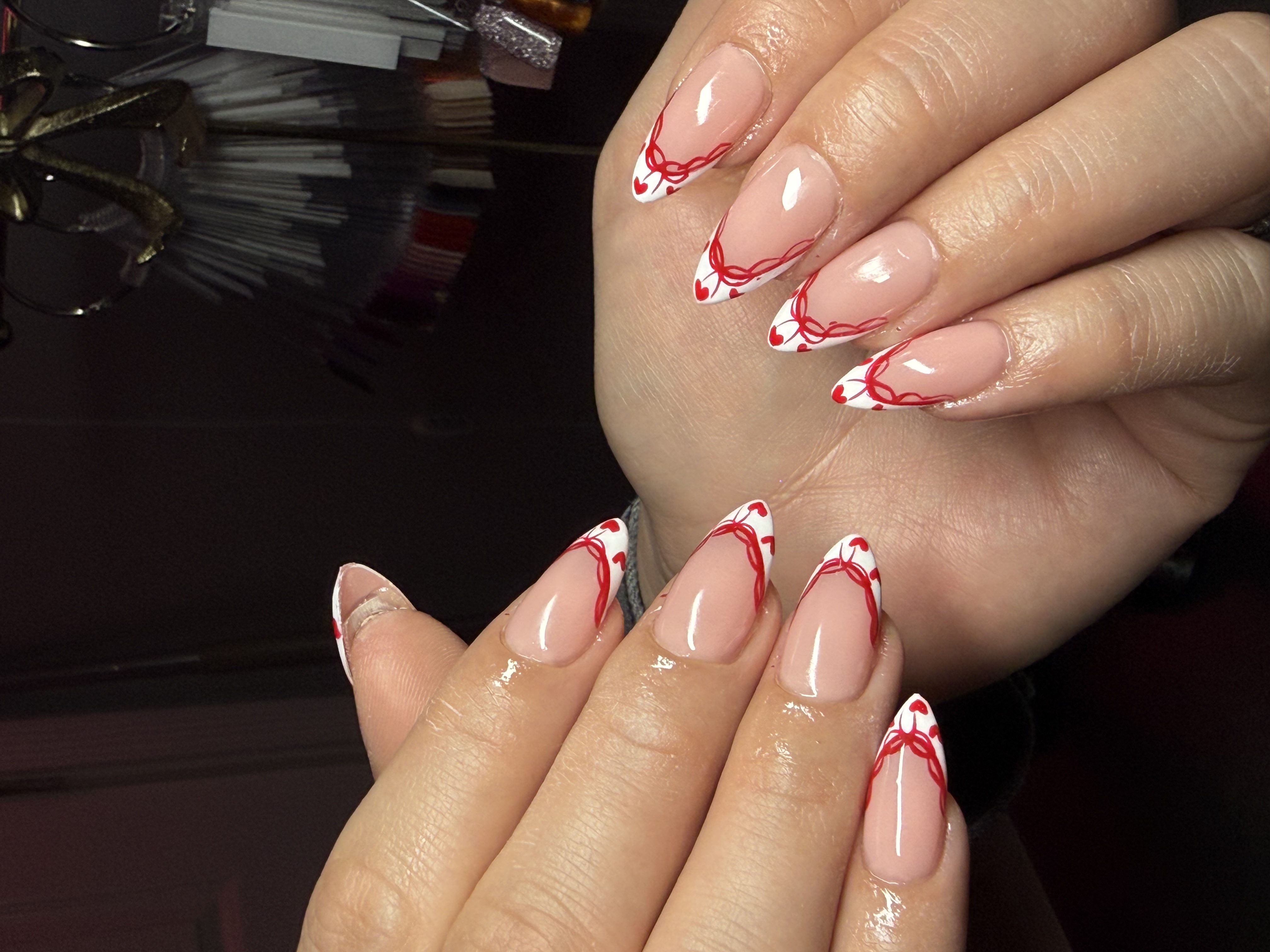 Almond french nails with intricate red ribbon corset lines and mini heart accents