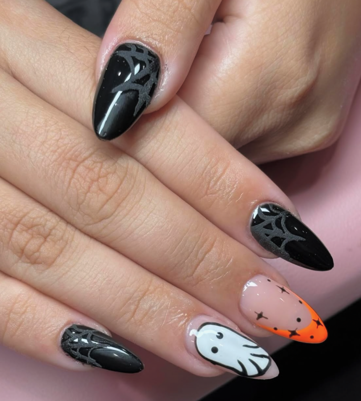 Midnight black stiletto nails with matte spiderwebs, neon orange french tip with star accents, and a cute ghost nail