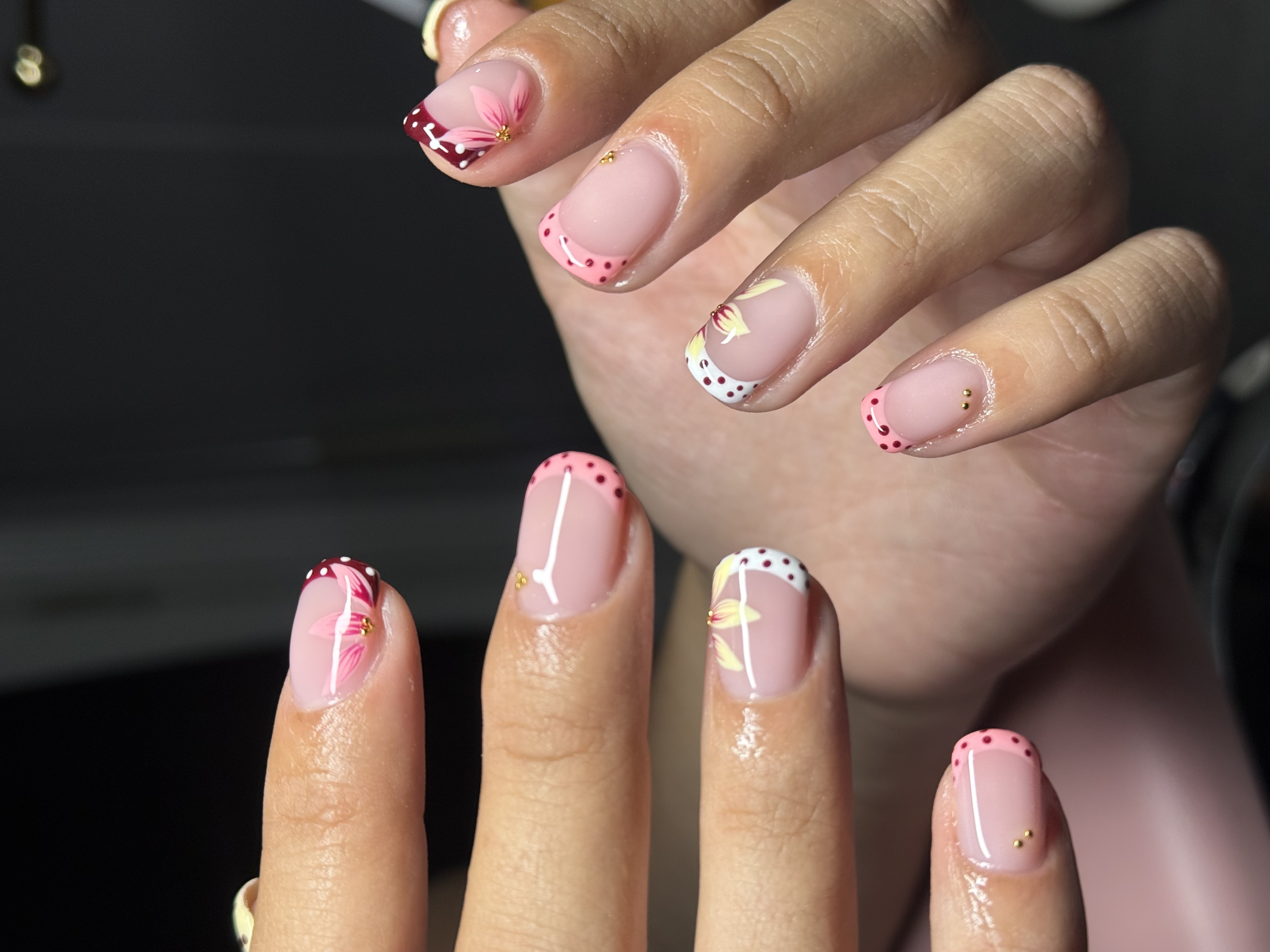 Short square nails with hand-painted blush cherry blossoms, polka dot tips, and gold studs