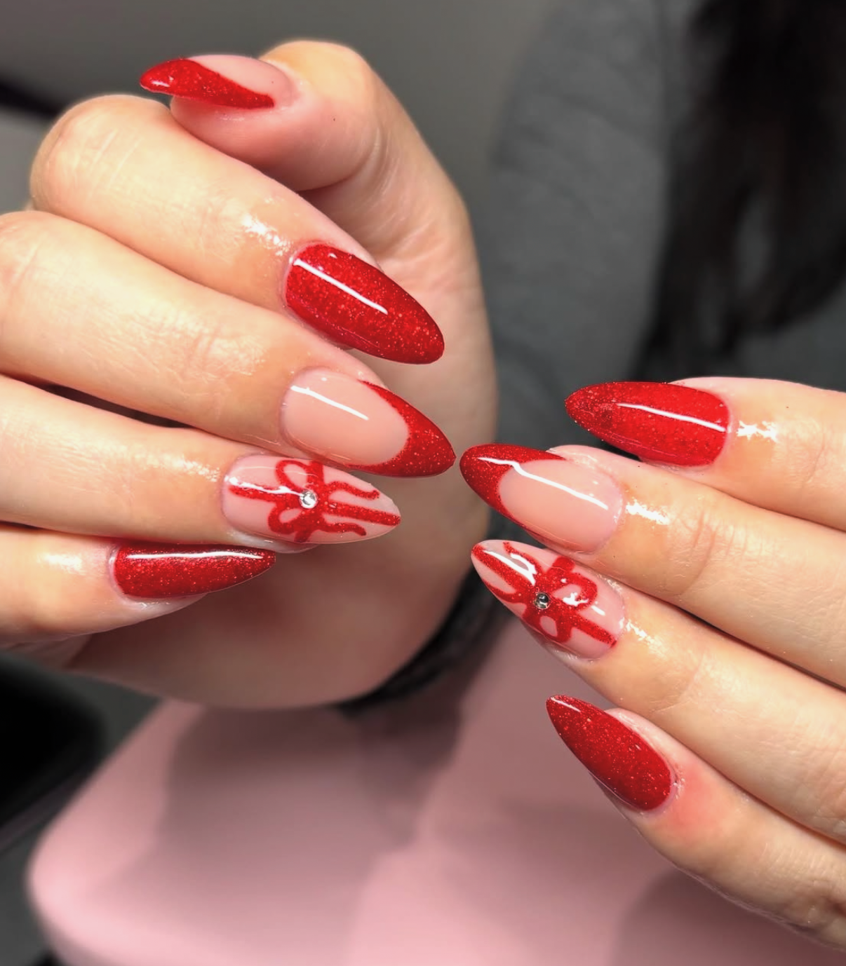Ruby red glitter stiletto nails with hand-painted crimson 3D bows and center rhinestone crystals