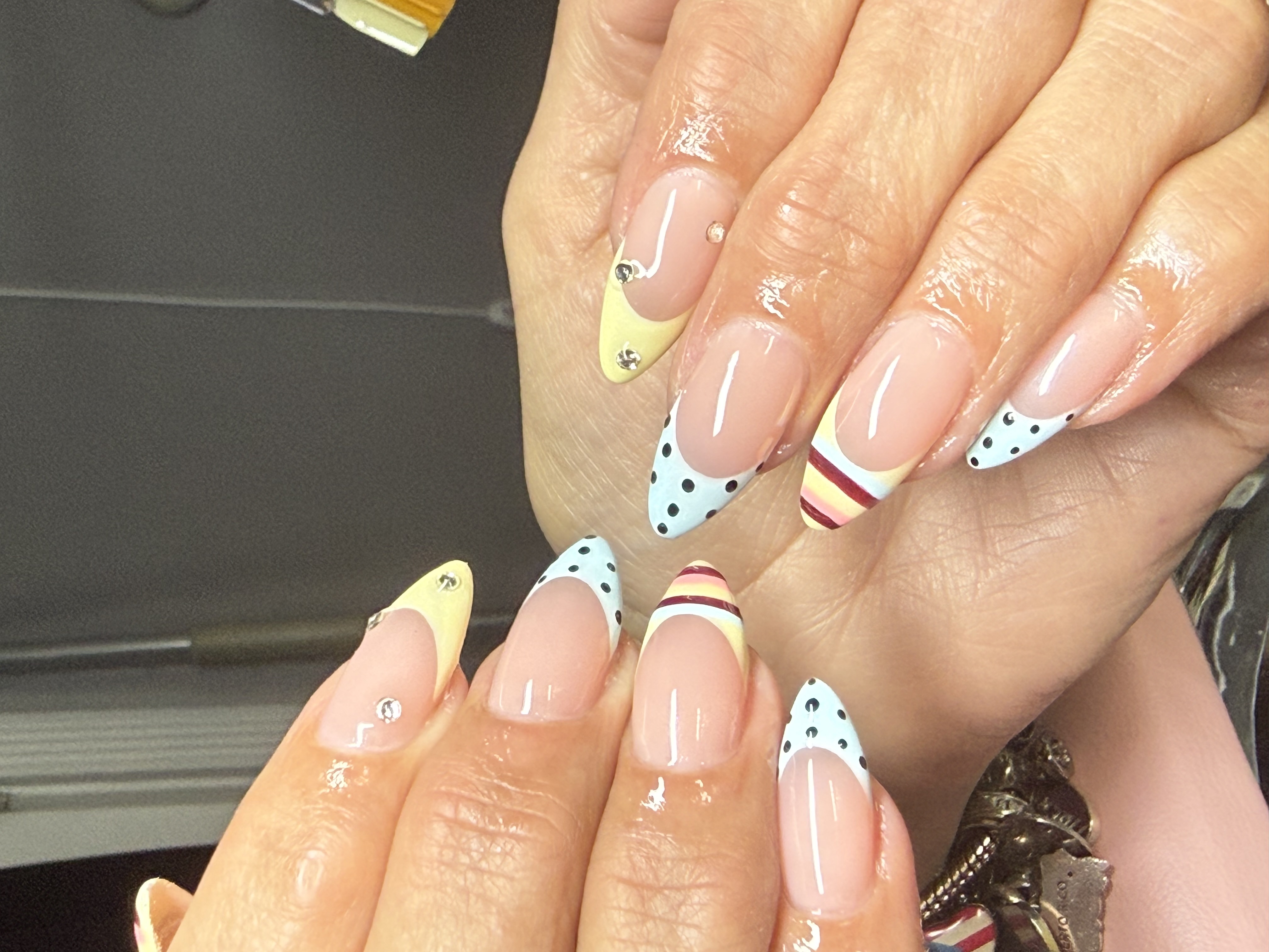 Almond nails featuring pastel yellow and sky blue polka dot french tips with crystal gems