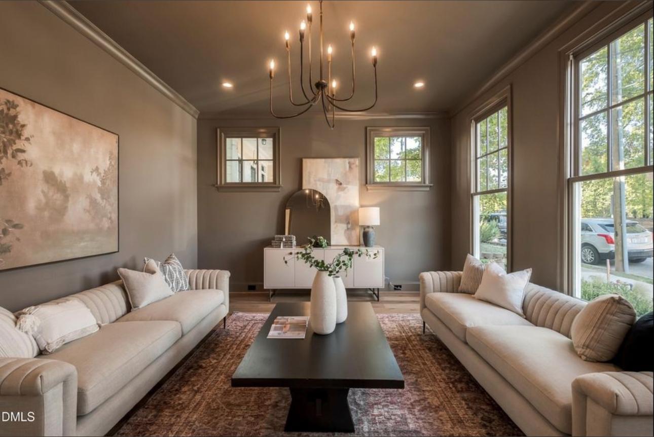Warm, sophisticated living salon with taupe color-drenched walls, fluted linen sofas, brass chandelier, and floor-to-ceiling multi-pane windows