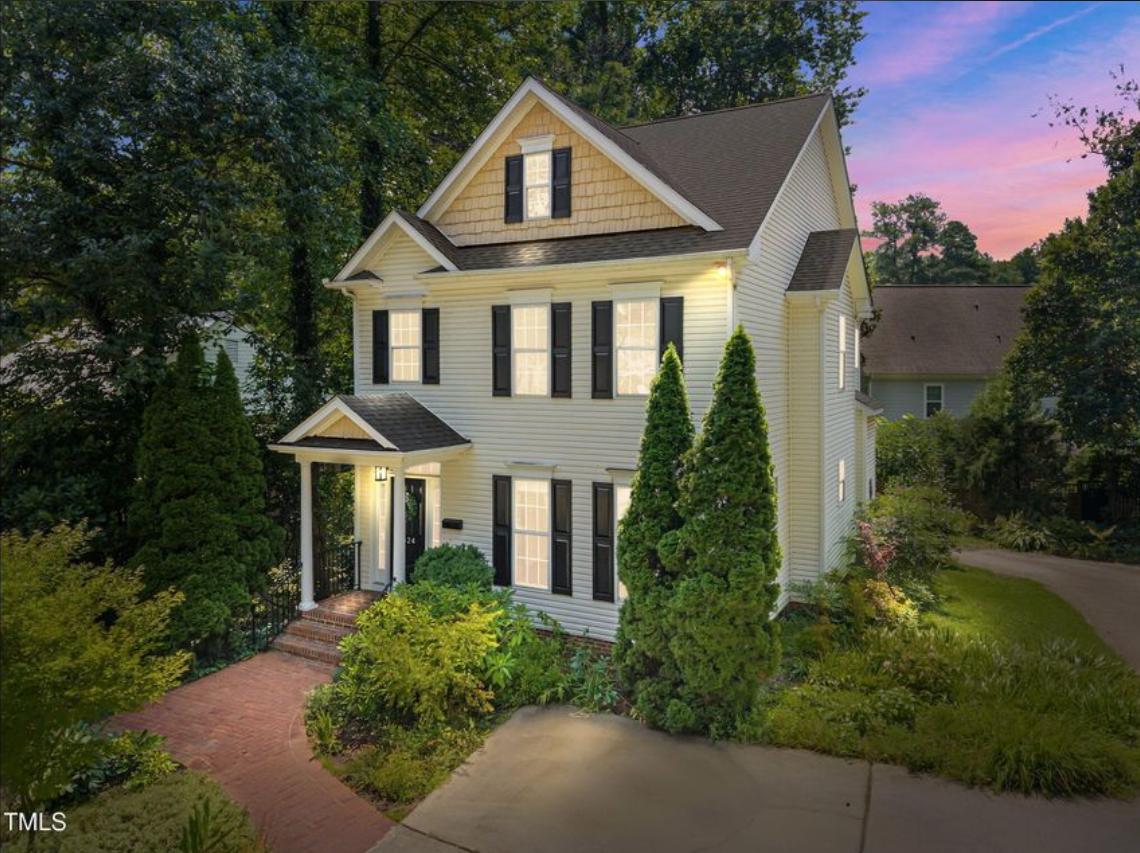 Three-story Raleigh craftsman home with brick walkway, manicured landscaping, and warm architectural lighting at sunset — represented and sold by Leah Beeson Real Estate