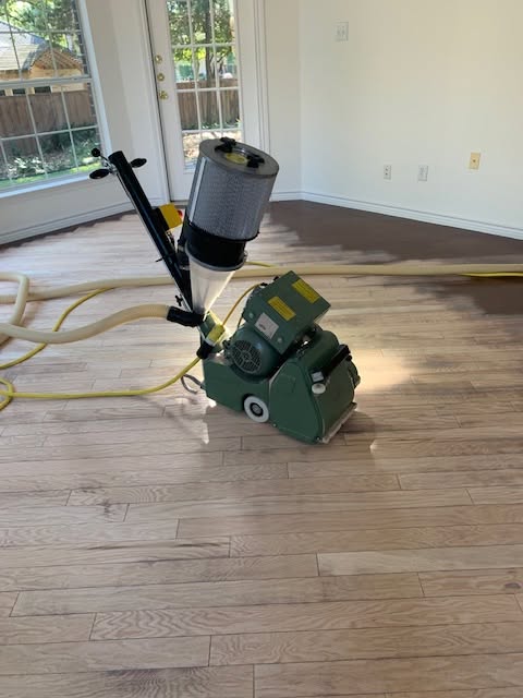 A hardwood floor craftsman sanding with a dustless sanding machine and dust-collection hose