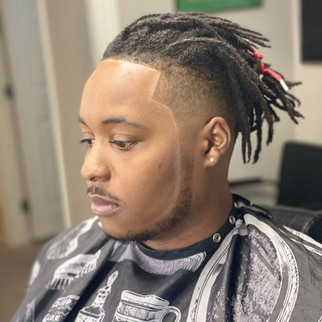 Locs styled back with mid taper fade and clean chalk-accented hairline