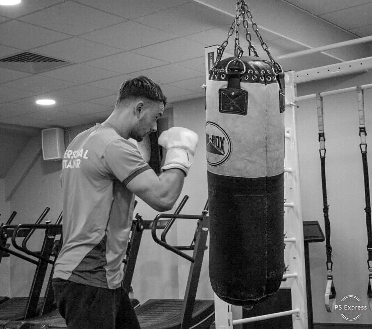 Tommy Rowlands boxing coach in Reading throwing a punch on the heavy bag in gym kit with boxing wraps and gloves