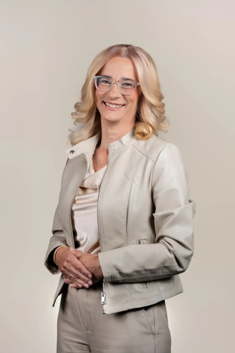 Mojca Sešlar v rožnatem suknjiču sedi na sivem stolu