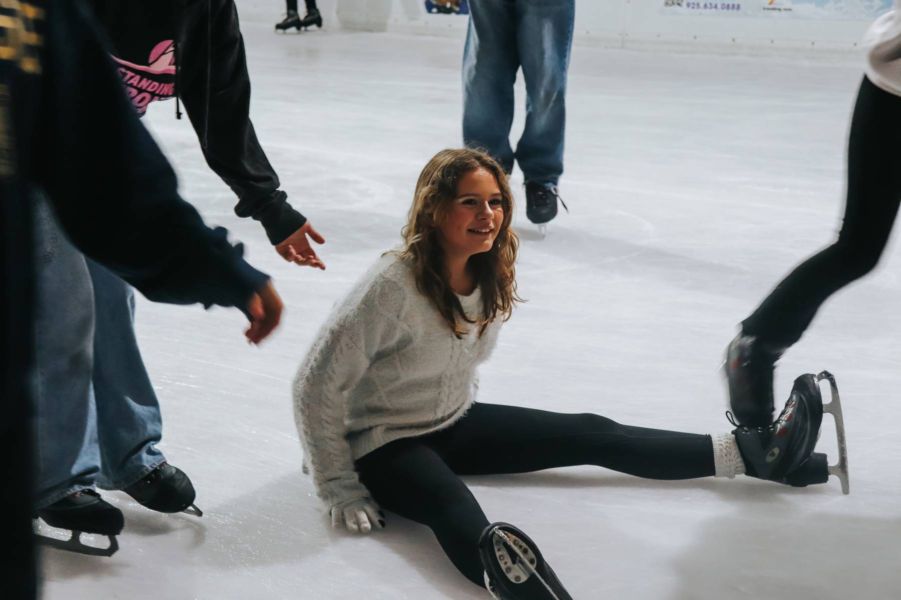 Smiling girl sitting on the ice rink having fun