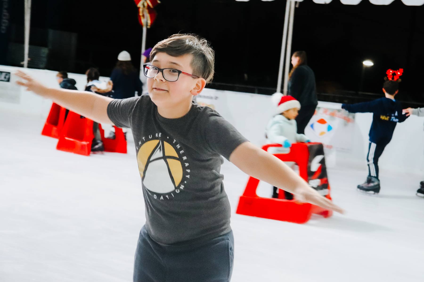 Young boy smiling and skating on the ice in an Adventure Therapy Foundation t-shirt