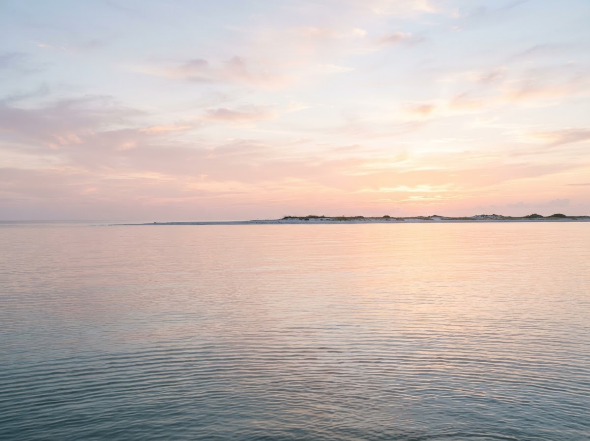 Calm pastel dawn over shallow Gulf water with a distant sandbar