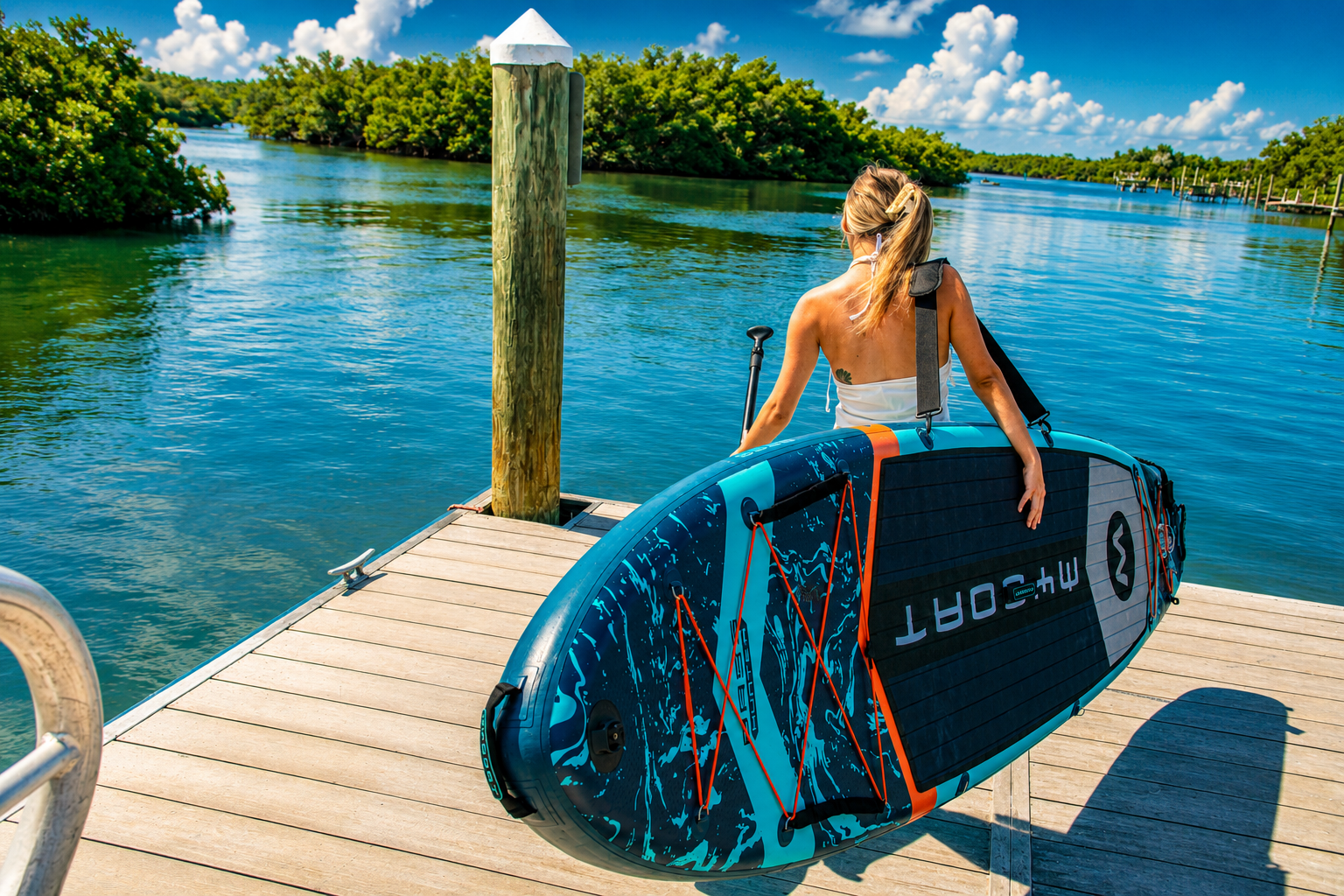 Paddleboarder carrying an inflatable stand up paddle board down the Weedon Island dock toward calm blue waters
