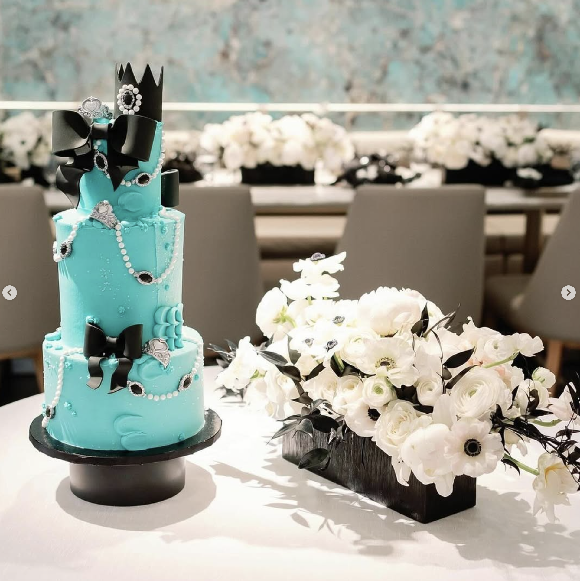 Couture celebration table with crisp white ranunculus, black foliage and tiered cake