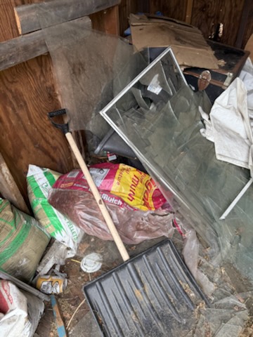 Storage shed cleanout with heavy window glass panes, mulch bags, and broken clutter in Chicopee MA